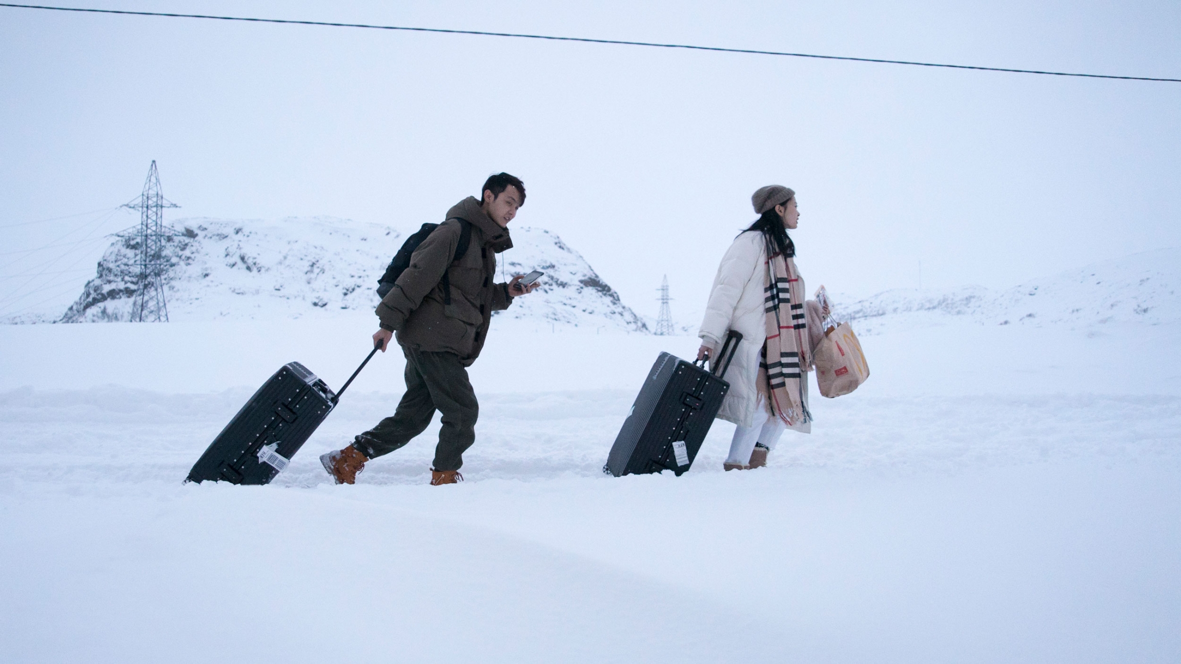 Chinese tourist pull their suitcases in Teriberka, Russia. Two people are shown pulling their suitcases amongst a snowy path.