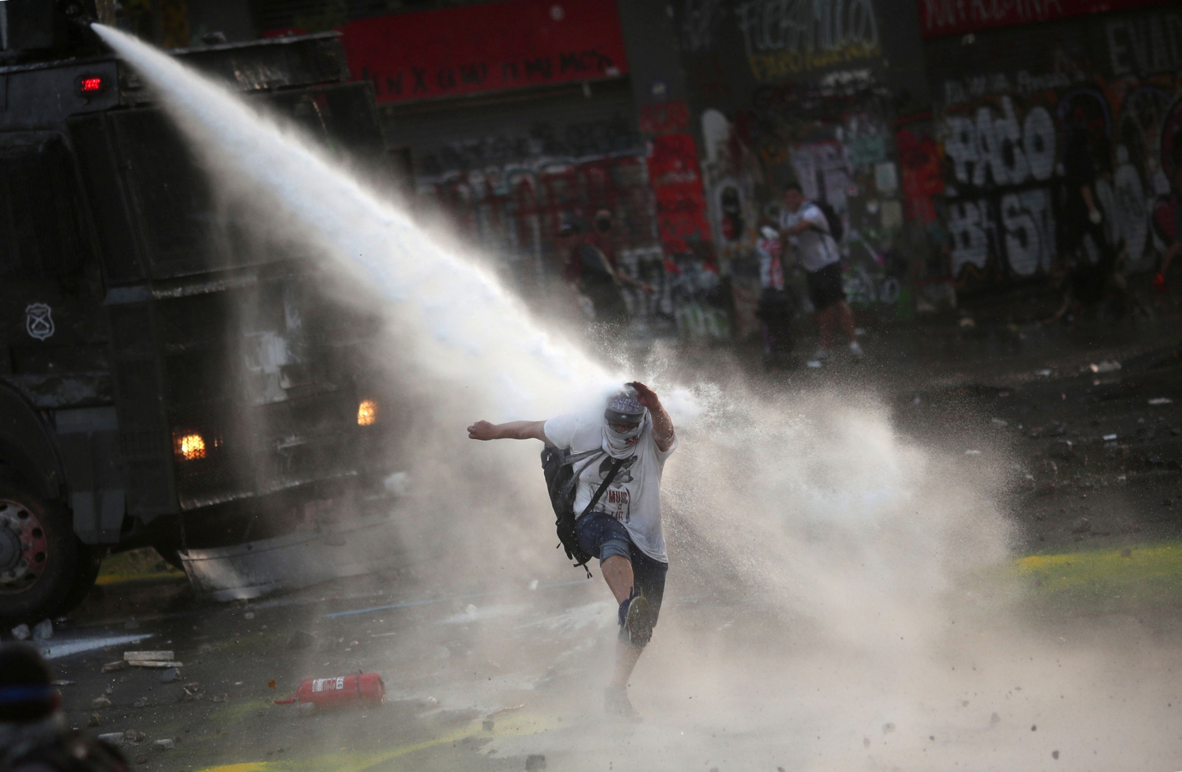 A demonstrator reacts as he is sprayed by a riot police water cannon during a protest against Chile's government in Santiago, Chile, Dec. 18, 2019. A person is shown being sprayed by a water cannon from above.