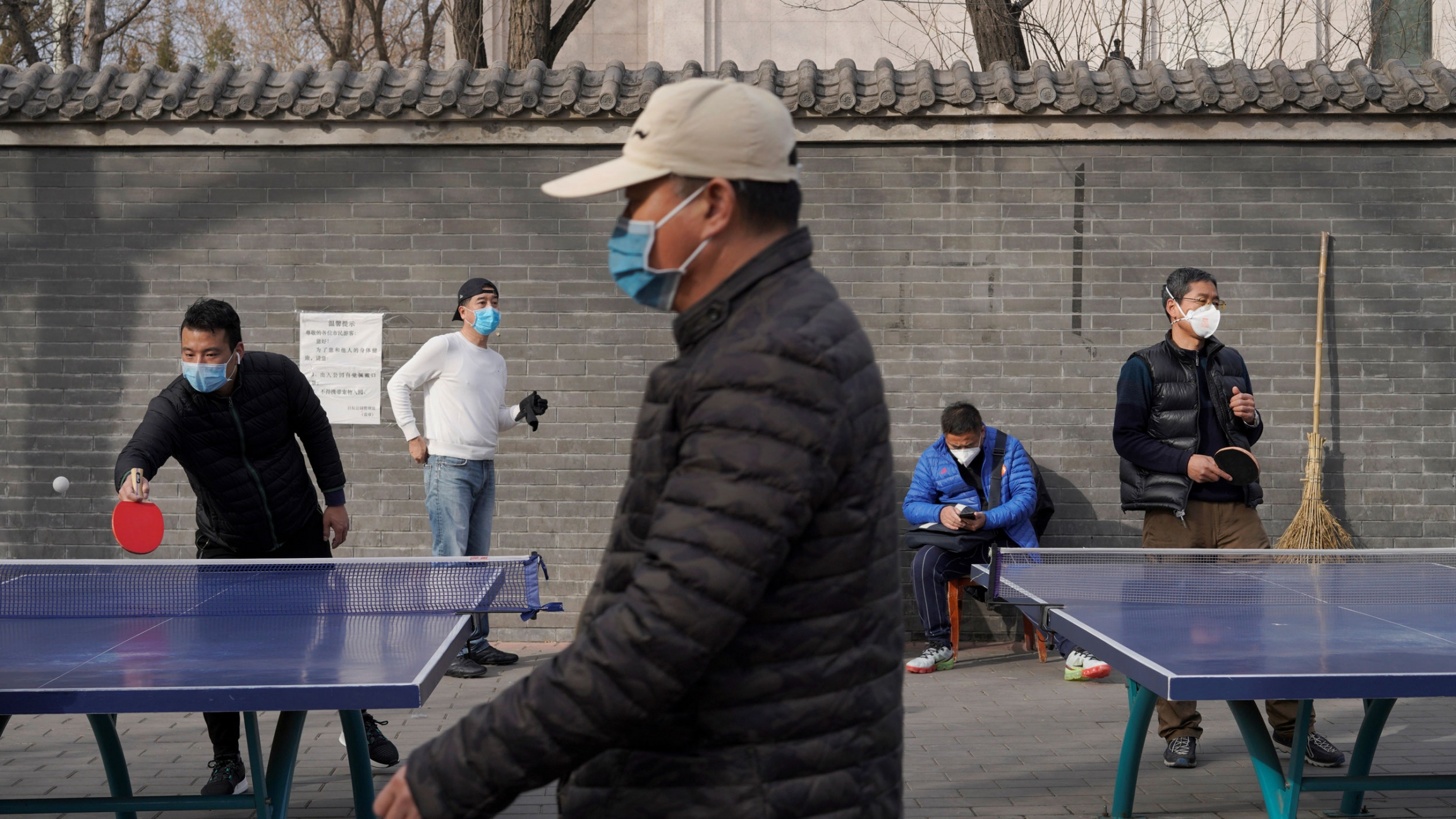 People wearing face masks play table tennis at a park, following an outbreak of the coronavirus in the country, in Beijing, China, Feb. 21, 2020. Several people are shown playing table tennis and wearing face masks.