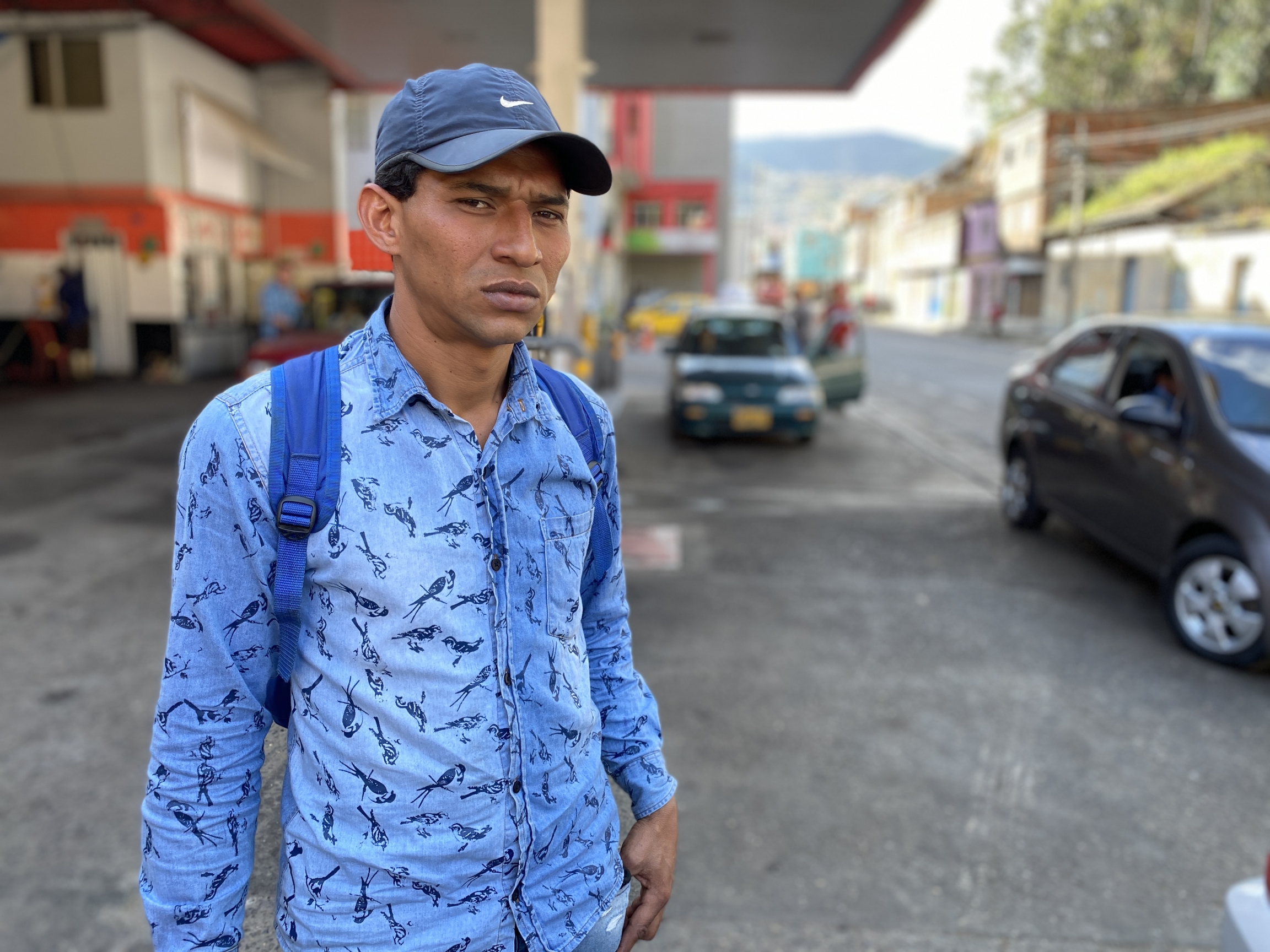 Former Venezuelan sergeant Javier Rivas poses for a photo in Pamplona, Colombia, Feb. 1, 2020. Rivas says he defected from the Venezuelan army because he no longer wanted to follow orders, which included harassing opposition politicians. A man wears a light blue button down shirt, backpack and Nike cap at a gas station.