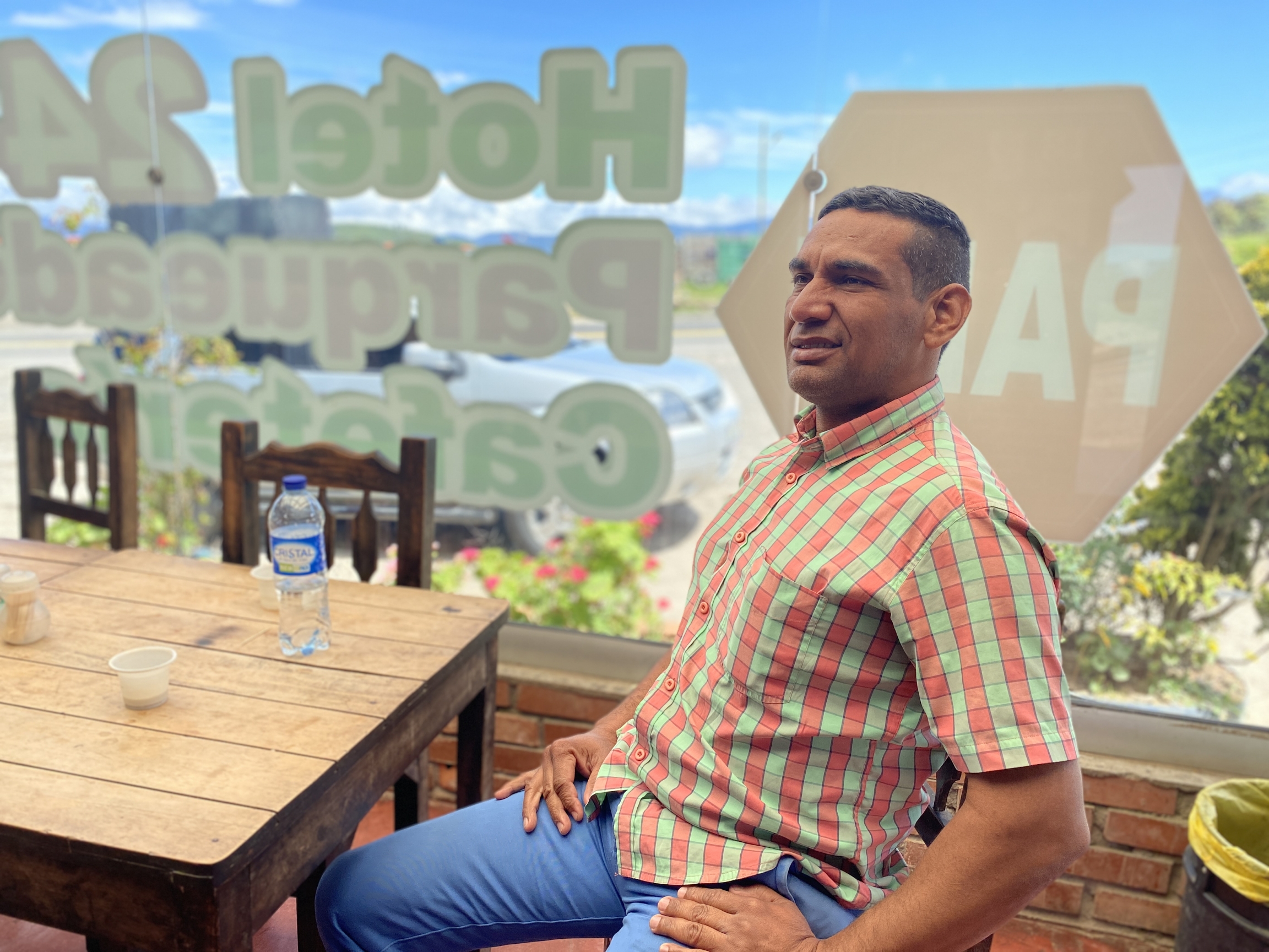 Yomalf Chavez Lugo has a drink in the outskirts of the Colombian city of Pamplona, Feb. 1 2020. Lugo says he has joined a group that is plotting to overthrow the Venezuelan government. A man sits at a table at a restaurant with a plastic bottle of water.
