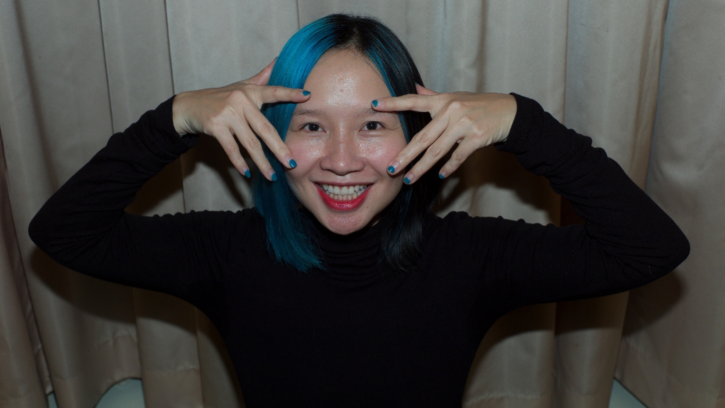 Vietnamese singer and songwriter Mai Khoi. A voman with her hair painted blue holds both or her hands by her eyes.