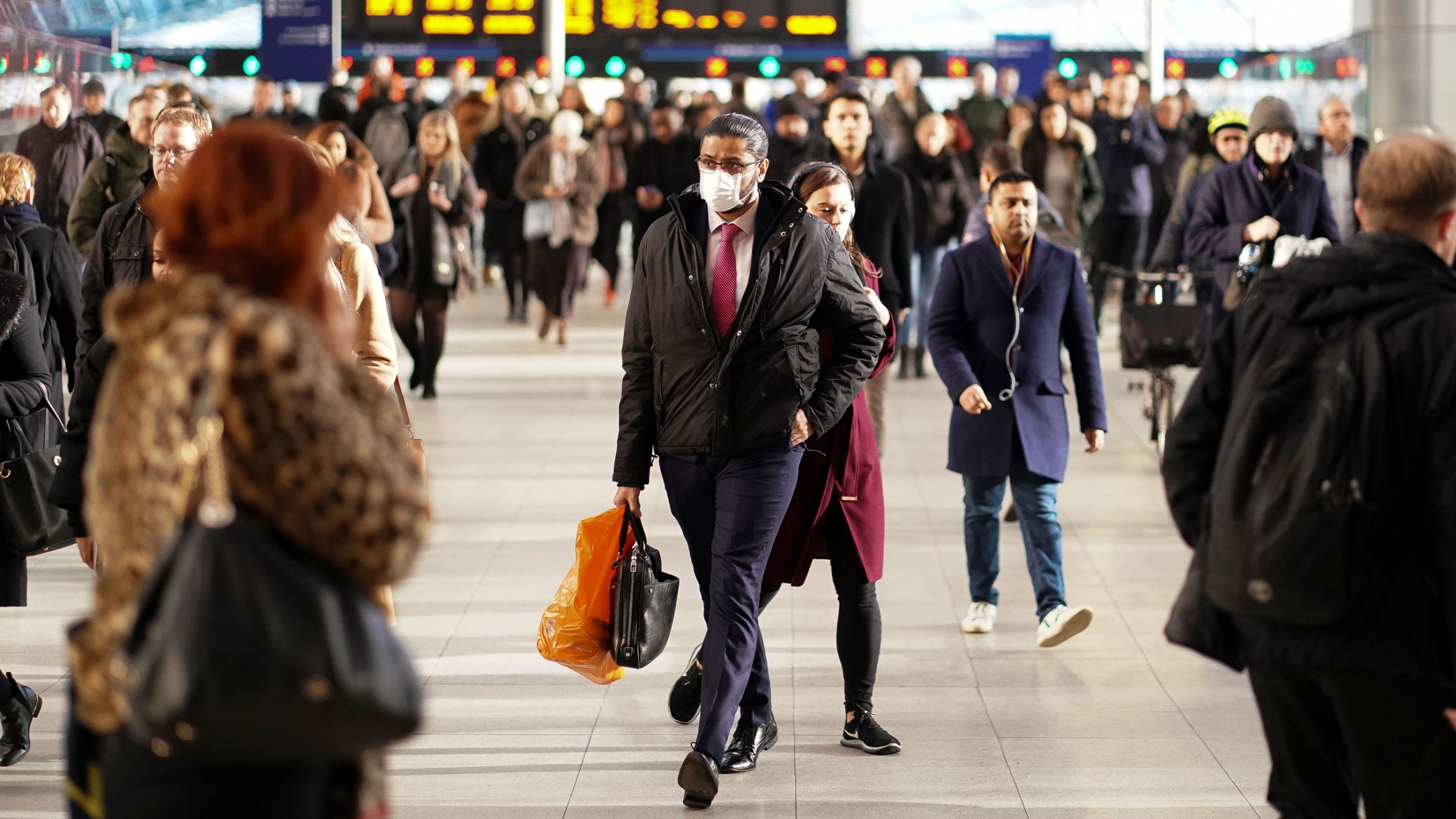 A man is seen wearing a protective face mask at Waterloo station in London, Britain, March 6, 2020. A large crowd of people are seen at Waterloo station with a man in the center of the frame wearing a face mask.