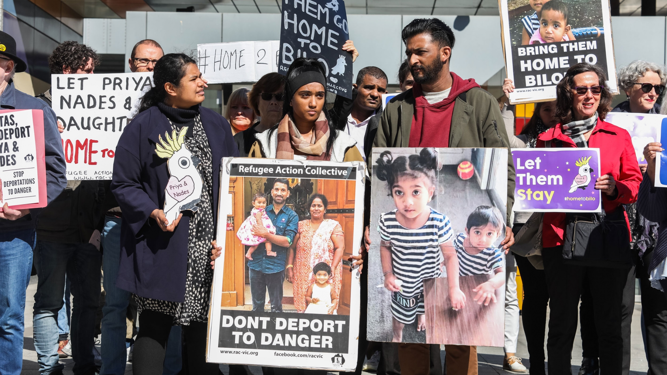Protesters outside a Federal court hold placards in support of a Tamil asylum seeking family in Melbourne, Australia. A group of protesters are shown holding placards with pictures of a Tamil family that includes the father, mother and their two small children.