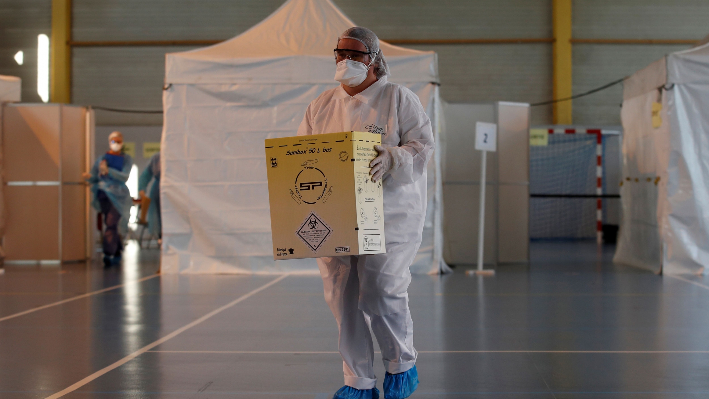 Medical staff, wearing protective suits and face masks, prepare material for medical consultations at an emergency COVID-19 center near Paris as the spread of the coronavirus continues in France, March 26, 2020. A medical worker is shown wearing a full protective suit and face mask and carrying a box of medical supplies.