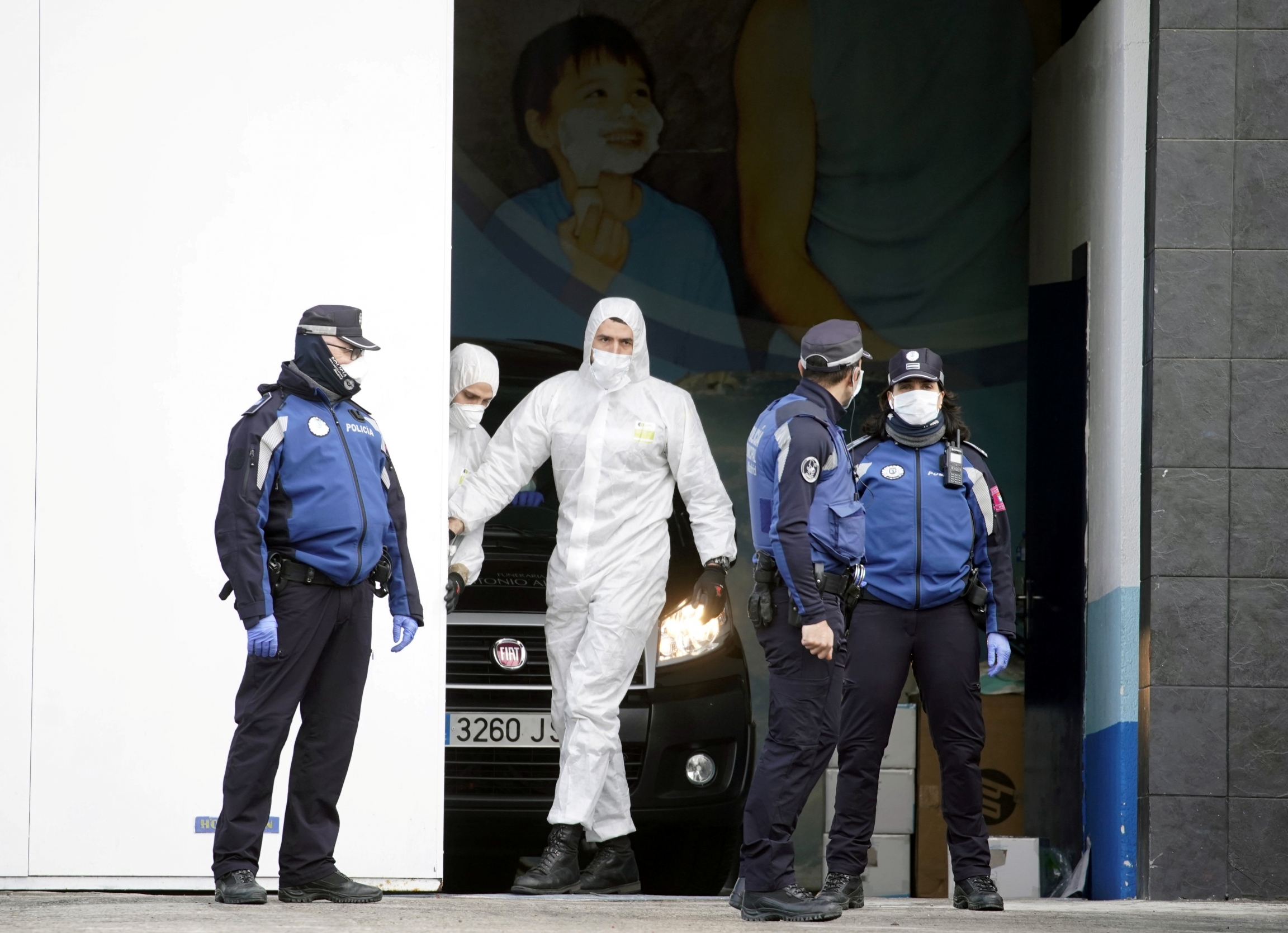 Local police stand next to a mortuary car, allegedly carrying the corpse of a person who died of the coronavirus disease (COVID-19), at the entrance of an ice rink which will be used as a morgue. Men in protective gear to load a corpse into a vehicle.