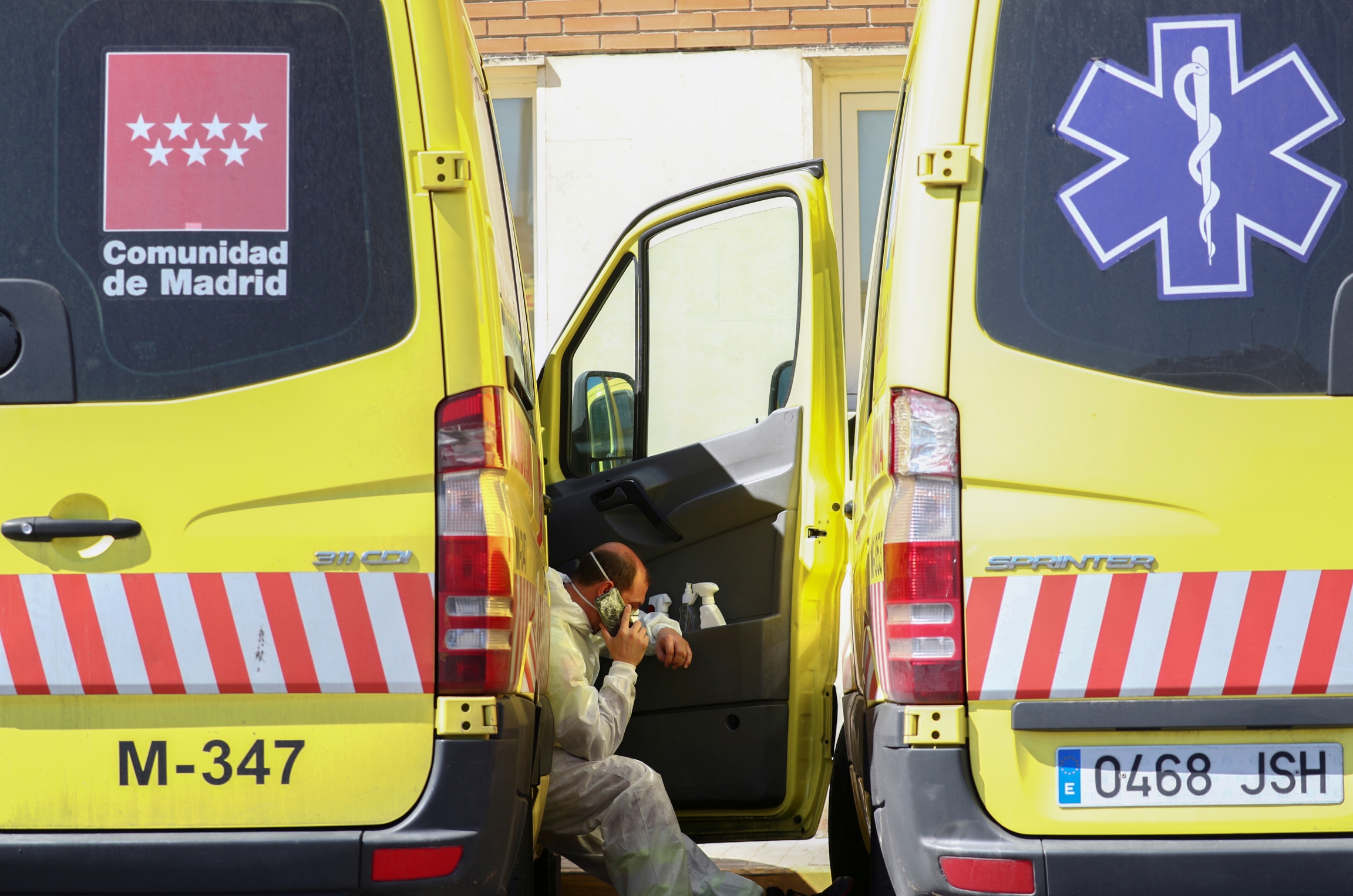 An ambulance driver wearing a protective face mask and suit takes a break near the emergency unit at 12 de Octubre hospital during the coronavirus disease (COVID-19) outbreak in Madrid, Spain March 28, 2020. An ambulance driver rests between two vehicles and talks on the phone
