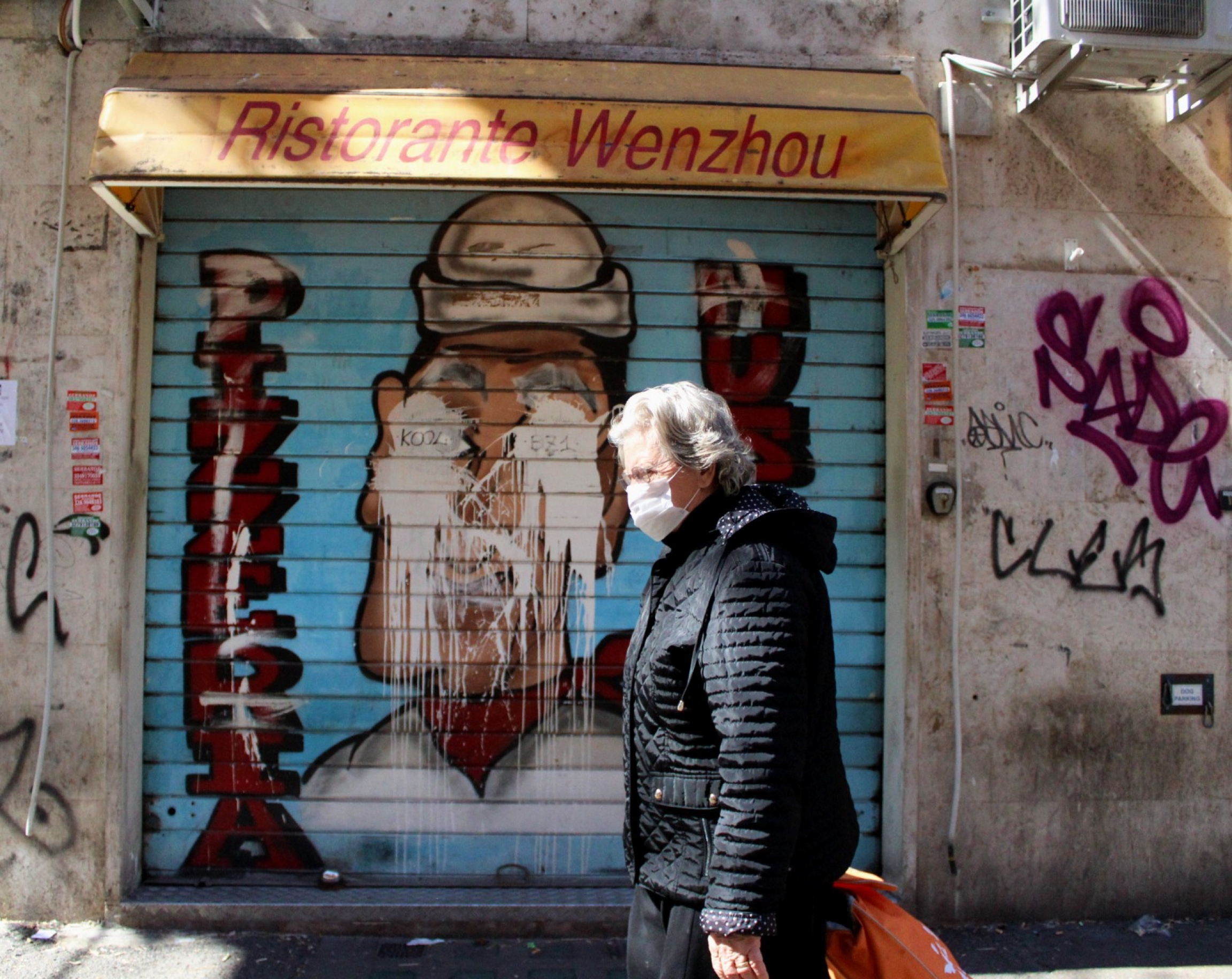 A woman wearing a mask walks by a popular Chinese restaurant in Torpignattara, Italy. A woman wearing a mask walks by a popular Chinese restaurant in Torpignattara, Italy.