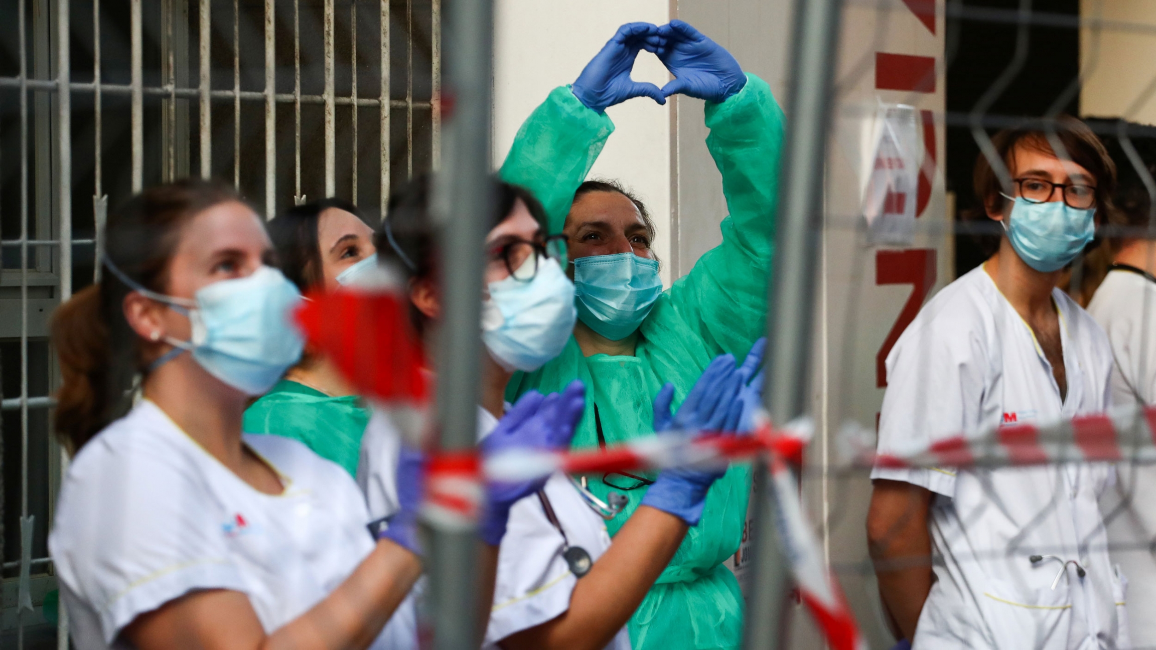 Medical staff from La Princesa hospital react as neighbors applaud from their balconies in support for healthcare workers, amid the coronavirus outbreak, in Madrid, Spain, April 5, 2020. Several health care workers are shown wearing protective suits and one woman making a heart shape with her hands.