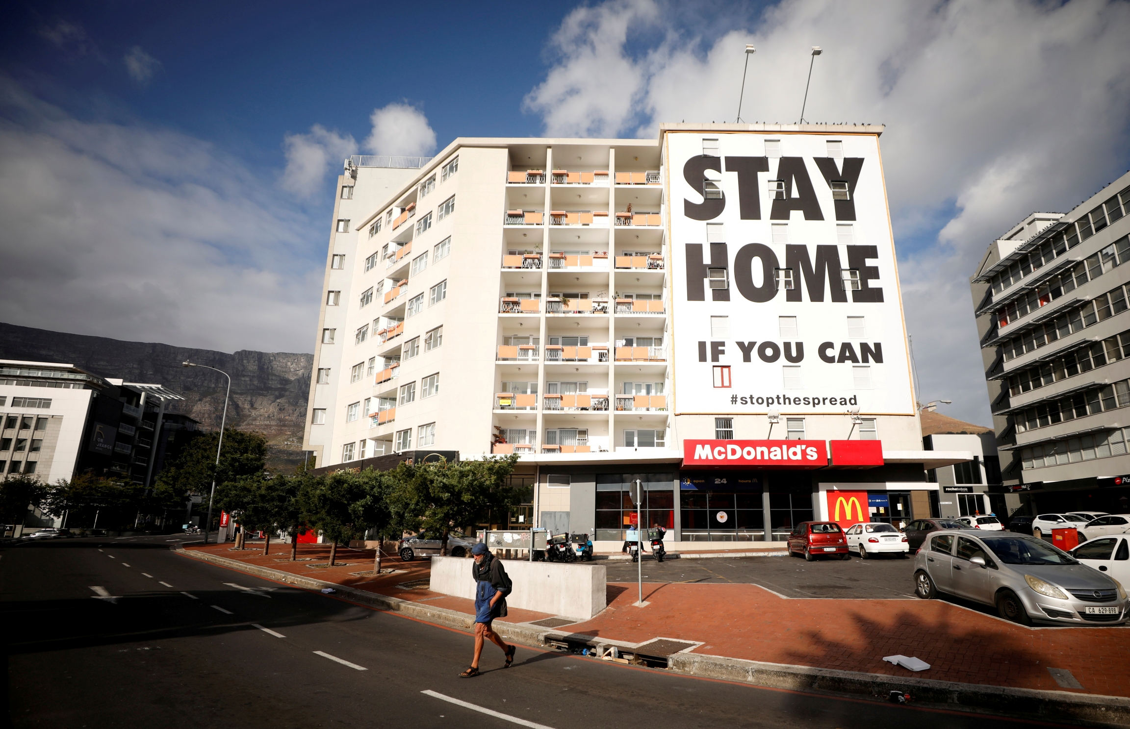 A man walks past a poster covering the side of a building ahead of a 21-day lockdown aimed at limiting the spread of coronavirus disease (COVID-19), in Cape Town, South Africa, March 26, 2020. Stay at home sign in South Africa