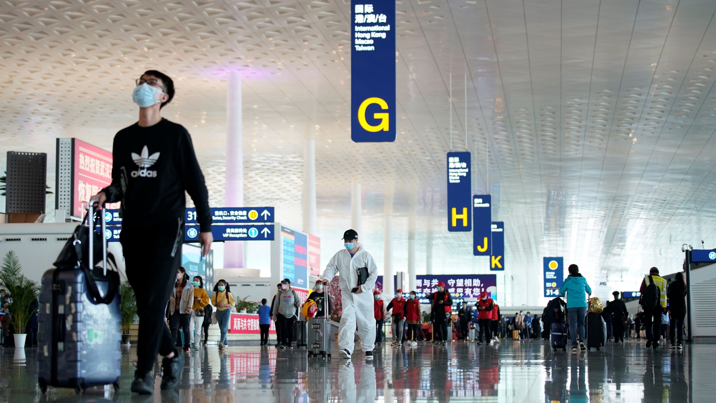 Travelers are seen at the Wuhan Tianhe International Airport after restrictions to leave Wuhan, China's epicenter of the novel coronavirus outbreak, were lifted, April 8, 2020. A large airport departures area is shown with several passengers walking toward gate agents.