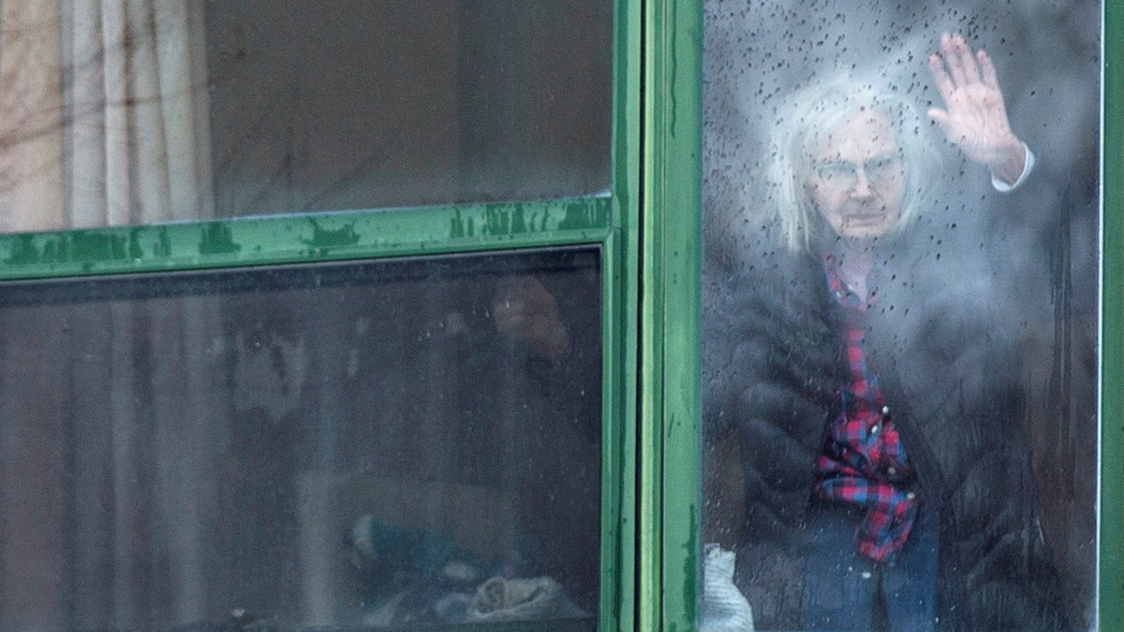 A resident waves from her window at Residence Herron, a senior's long-term care facility, following a number of deaths since the coronavirus outbreak near in Montreal, Canada, April 13, 2020. A woman is shown through the glass of a window with her had on the glass.