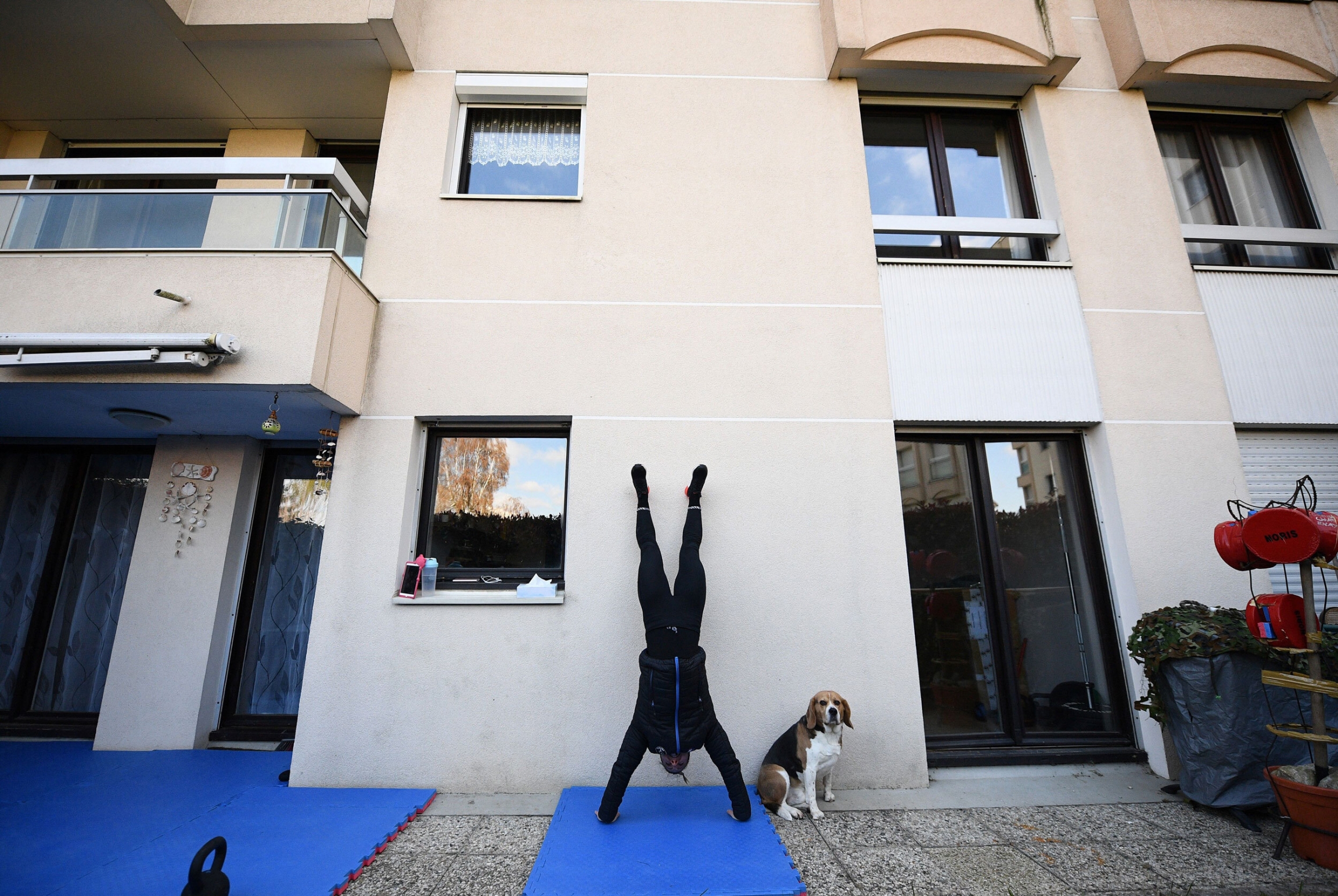 Alexandre Recchia training in her home near Paris during coronavirus-induced quaratine. A woman on black gym clothes does a hand-stand on a mat in her backyard.