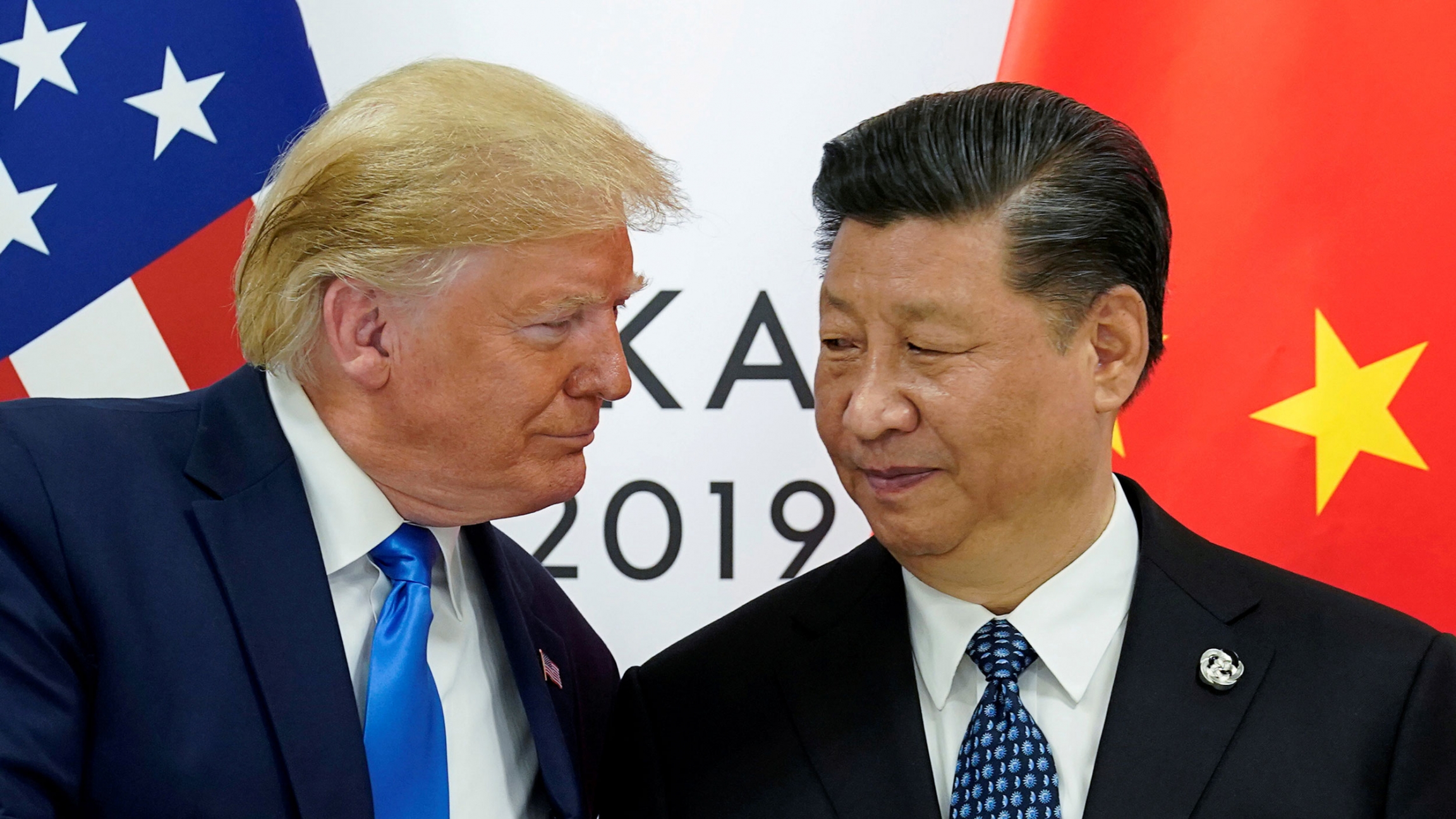 US President Donald Trump and China's President Xi Jinping are shown at the start of their bilateral meeting at the G20 leaders summit in Osaka, Japan, June 2019. US President Donald Trump and China's President Xi Jinping are shown both wearing dark suits and ties while standing in front of the US and Chinese flags.