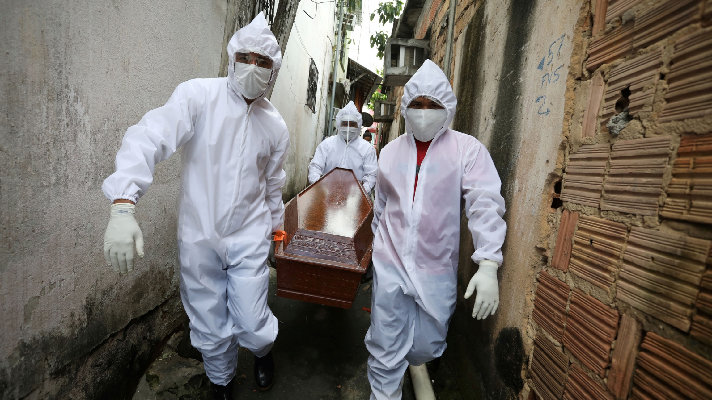 Workers, wearing protective clothing, carry the coffin of Vandir da Costa, from his house amid the coronavirus outbreak, in Manaus, Brazil May 7, 2020. Three workers are shown wearing white medical protective clothing and masks while carrying a wooden coffing in a small alley.