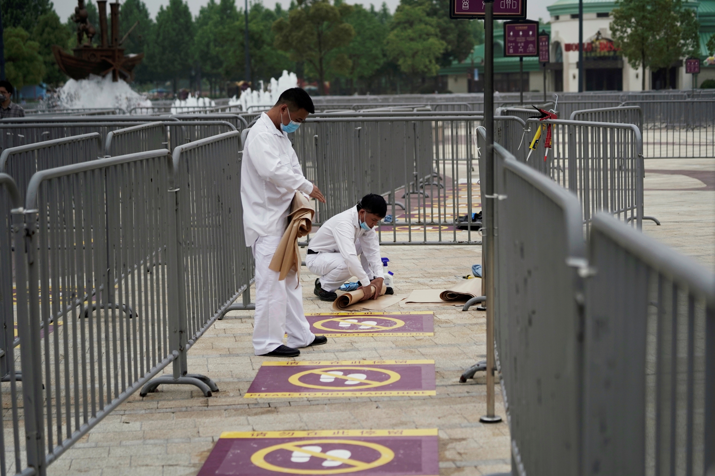Workers wearing face masks prepare social distancing markers at Shanghai Disney Resort a day before the Shanghai Disneyland theme park reopens following a shutdown due to the coronavirus disease (COVID-19) outbreak, in Shanghai, China, May 10, 2020. Workers wearing face masks paint social distance markers on the ground at Shangahi Disneyland