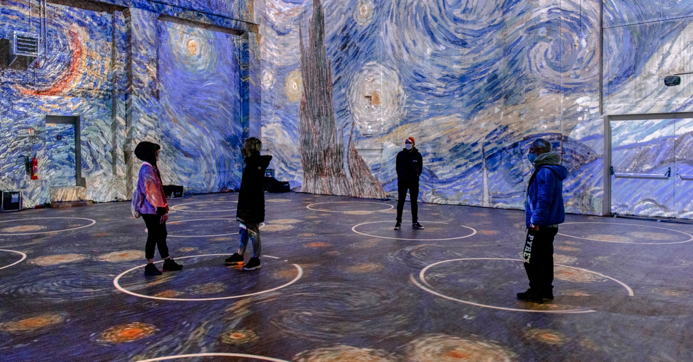 A photo mock up of Van Gogh art projected in a space with people standing in "social distance circles."