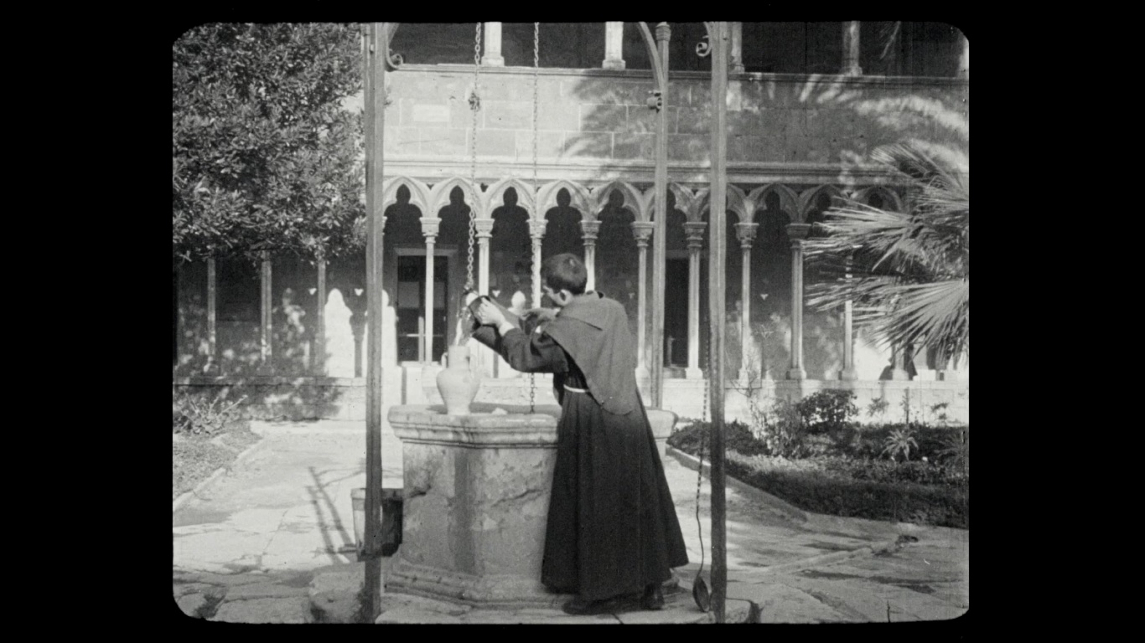 A scene from "Mallorca," made by María Forteza, the first female director of a talking film in Spain. A man in a religious robe near a well in black and white
