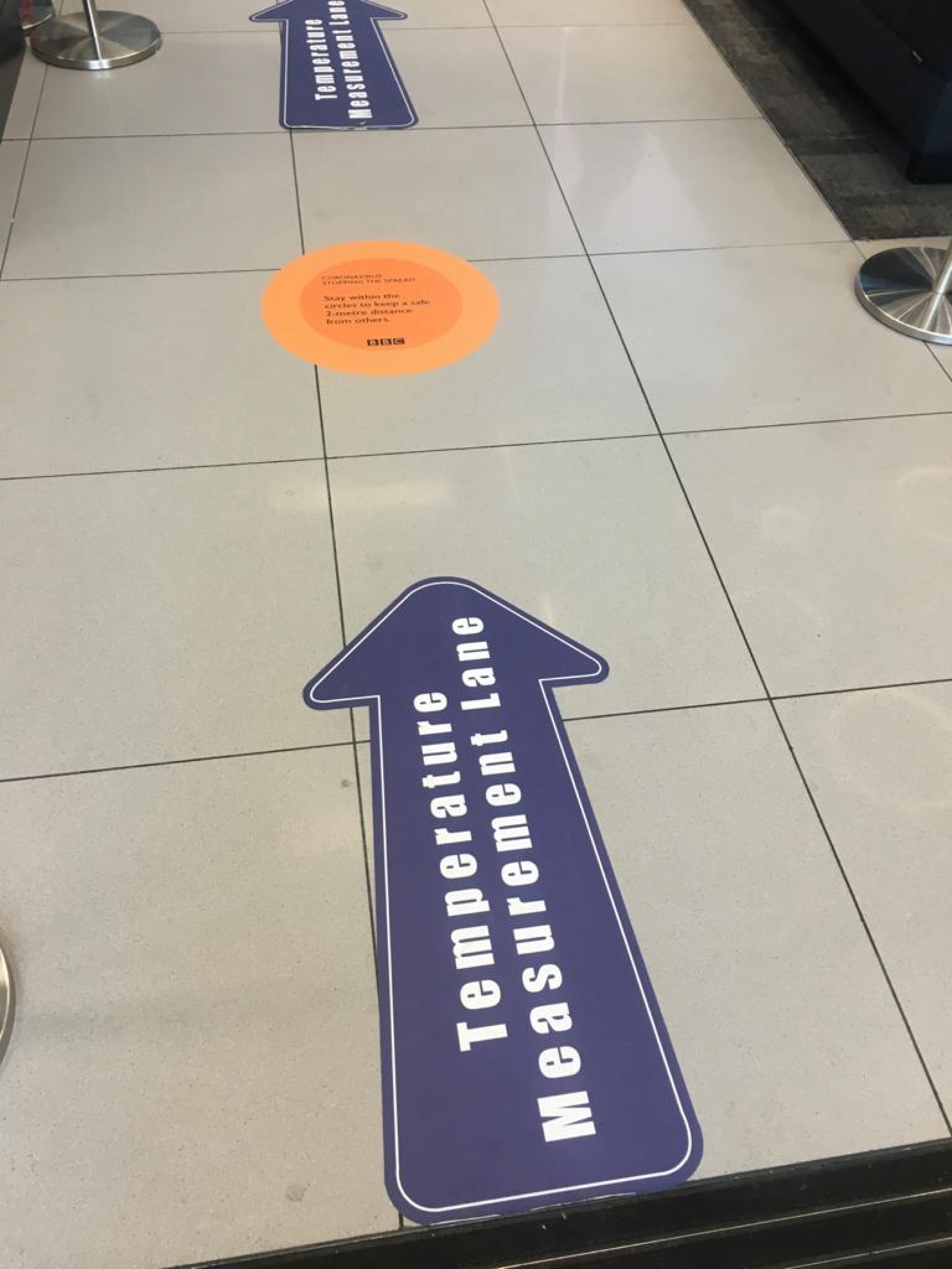 Signs on the floor at the BBC direct people to the thermal scanners. Signs on the floor at the BBC direct people to the thermal scanners.