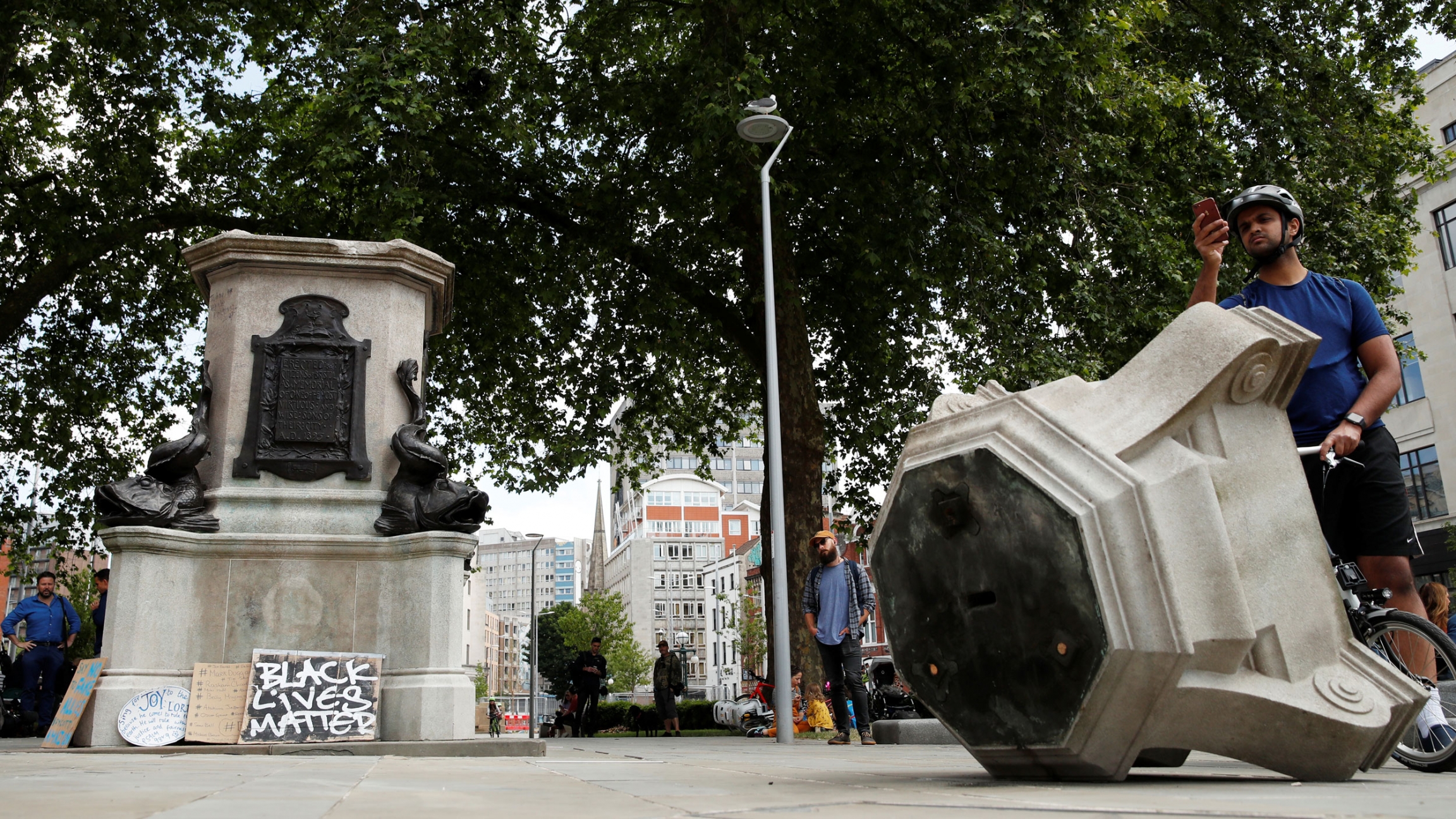 A man observes the base of the statue of Edward Colston, a slave trader in the 17th century, after protesters pulled it down and pushed into the docks, following the death of George Floyd, Bristol, Britain, June 8, 2020. The broken remains of a statue are shown in a small courtyard with a man taking a cell phone photograph in the background.