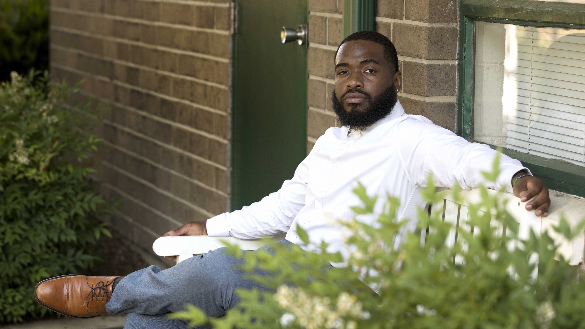 As an Afro Latino with roots in Honduras, Brayan Guevara straddles two groups whose votes candidates are fighting to capture: Latinos and blacks. Guevara wants to make sure his voice is heard at the ballot box. A young ma with a beard sits in front of a house looking at the camera.