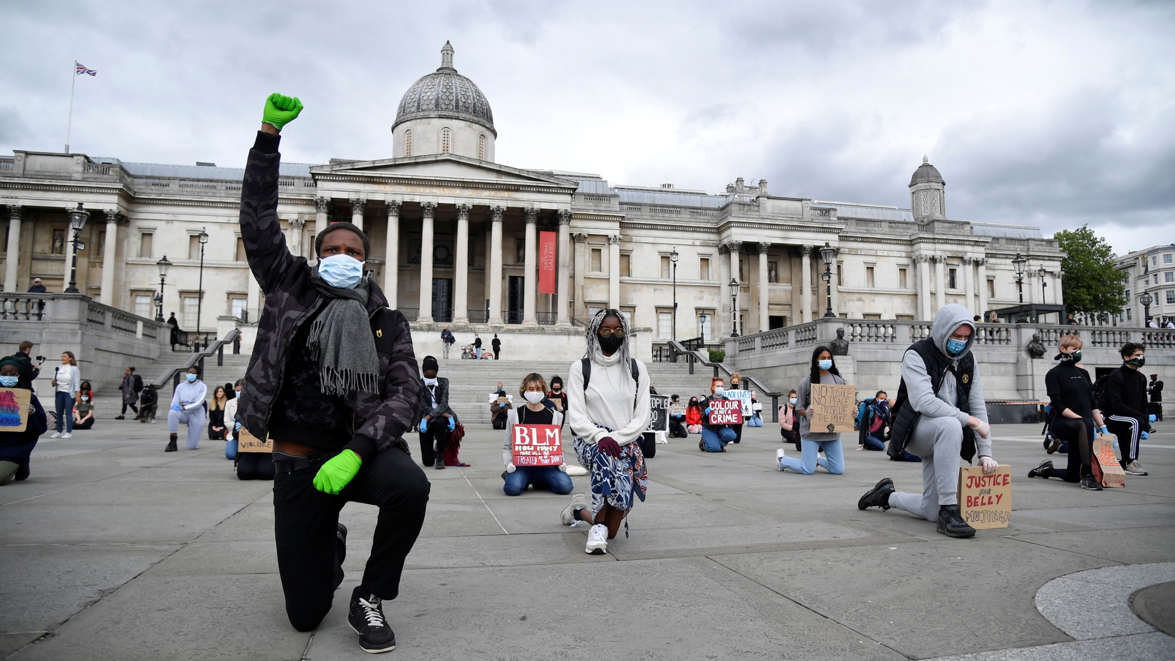 People wearing masks and holding signs kneel during a Black Lives Matter protest in Trafalgar Square in London, Britain, June 5, 2020. A large group of people are shown kneeling while spaced apart from each other in Trafalgar Square.