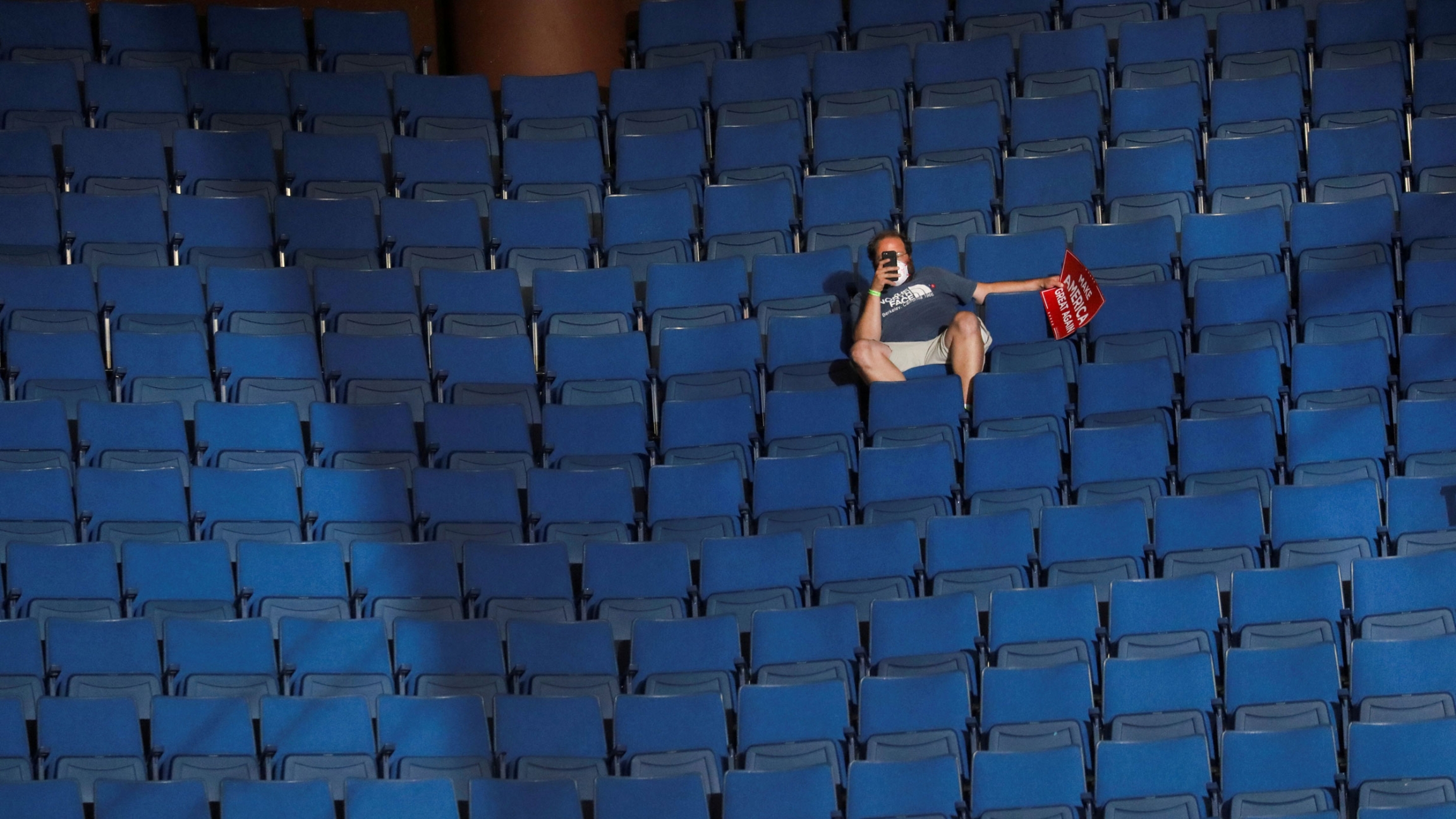 A supporter of President Donald Trump shoots a video with his phone from the sparsely filled upper decks at the BOK Center in Tulsa, Oklahoma, June 20, 2020. A man is shown sitting in a chairi in an arena hollding his phone up with empty rows of chairs all around him.