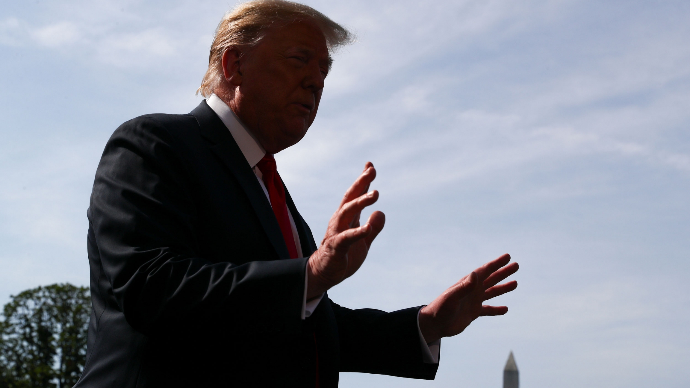 US President Donald Trump talks to reporters before boarding Marine One helicopter from the South Lawn of the White House in Washington, DC, June 23, 2020. US President Donald Trump is shown in shadow with his hands outstretch and the Washington Monument in the background.