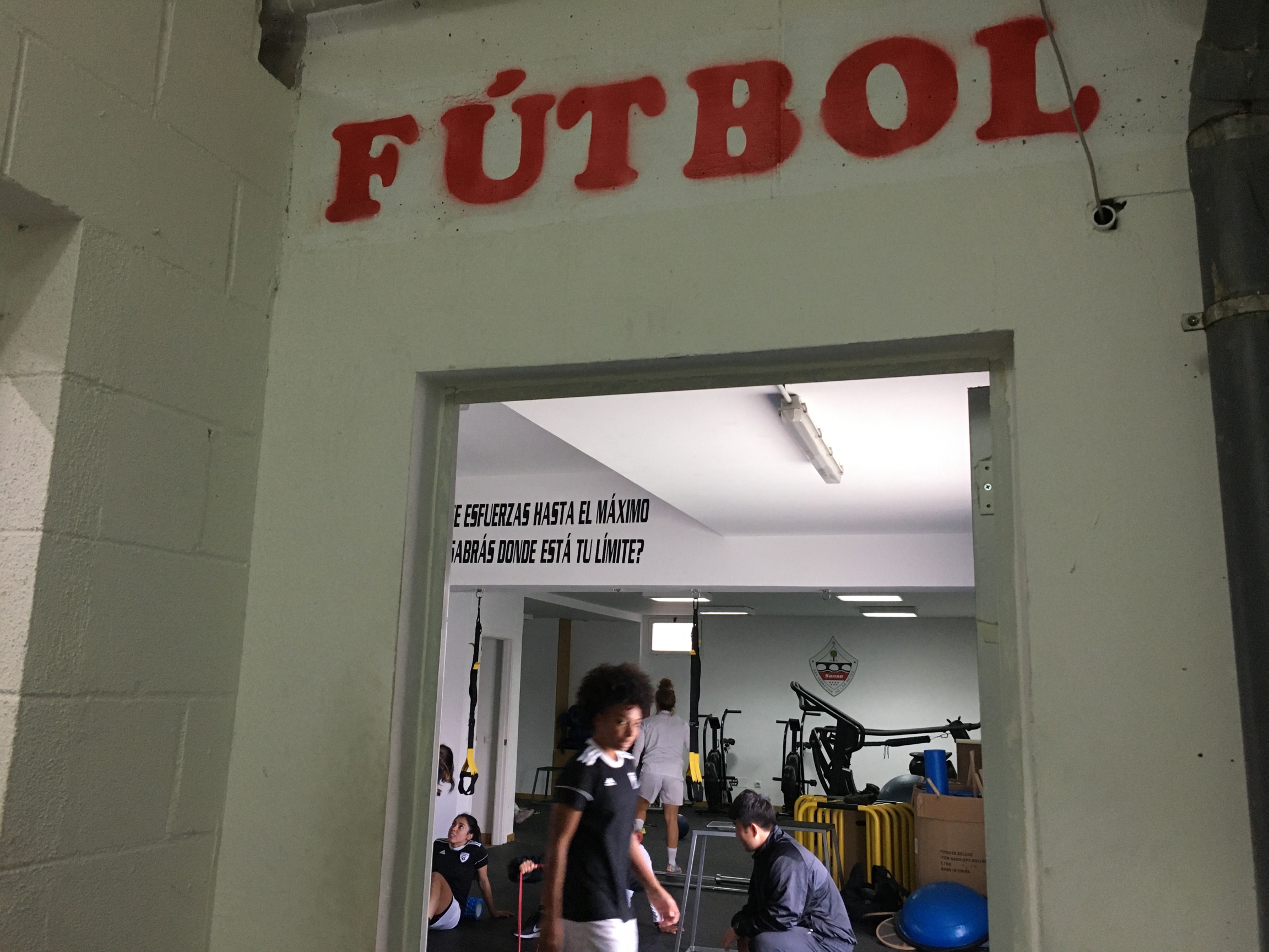 Madrid women's soccer players train together. Entrance to gym reads "Futbol" in red letters.