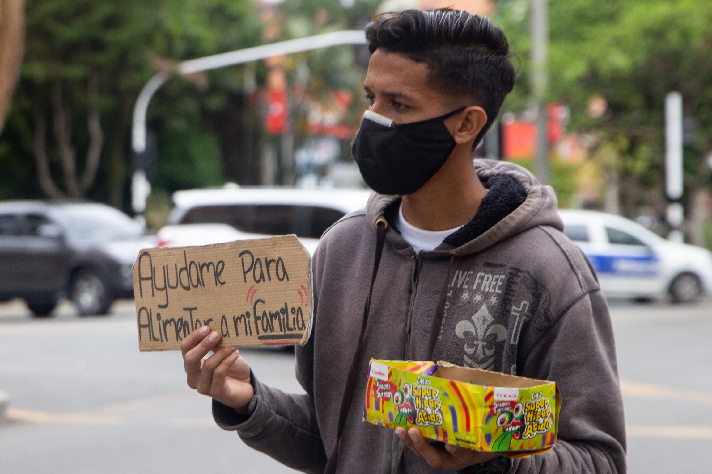 Miguel Benites 24, sells candies on the streets of Medellín, Colombia. He lost his job as a mechanic during the pandemic. A young man wearing a black face mask sells colorful candies on the street.
