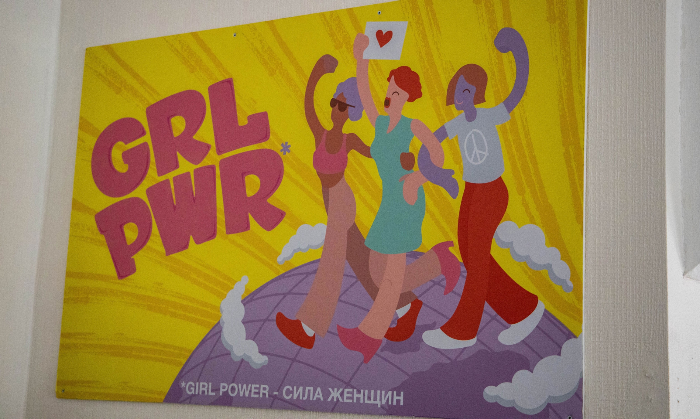 A poster promoting “girl power” hangs in Eve's Ribs in St. Petersburg. An illustrated poster shows three women linked arm in arm walking on a globe and it says GRL PWR.