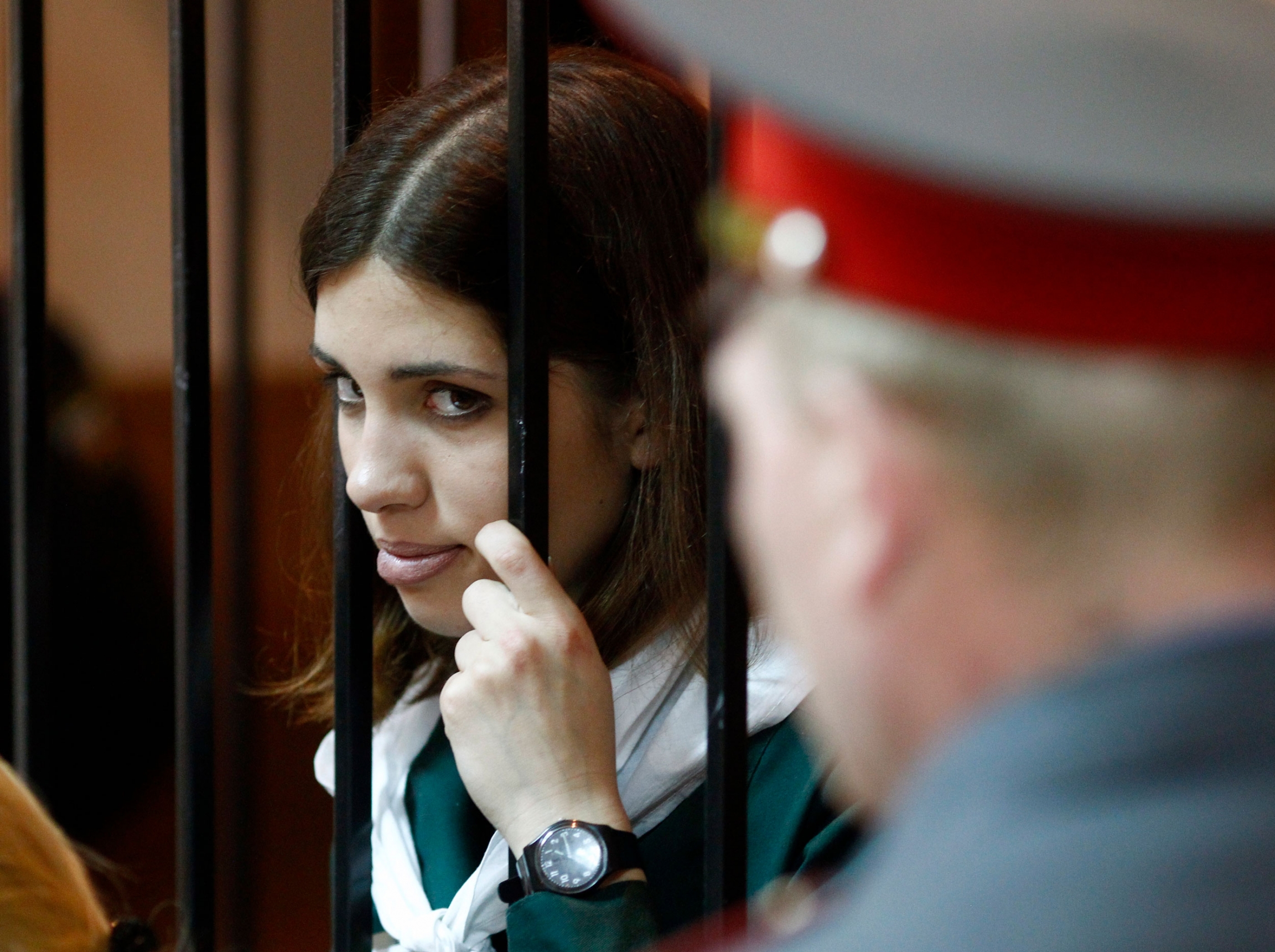 Pussy Riot band member Nadia Tolokonnikova looks out from a holding cell during a court hearing appealing her conviction for hooliganism in April 2013. A young woman holds bars of a cell and peers out in a courtroom