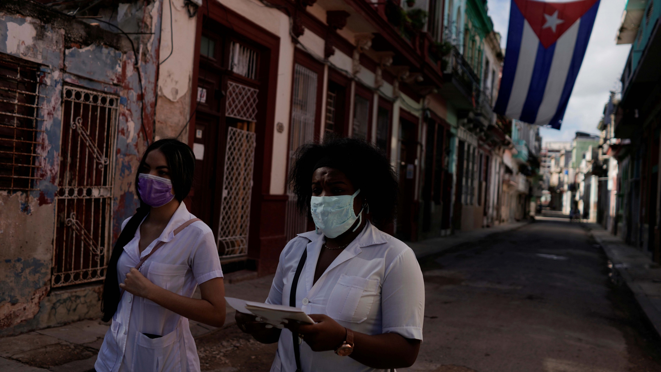 Medical students walk past a Cuban flag as they check door to door for people with symptoms amid concerns about the spread of the coronavirus disease (COVID-19), in downtown Havana, Cuba, May 12, 2020. Medical students walk past a Cuban flag as they check door to door for people with symptoms amid concerns about the spread of the coronavirus disease (COVID-19), in downtown Havana, Cuba, May 12, 2020.