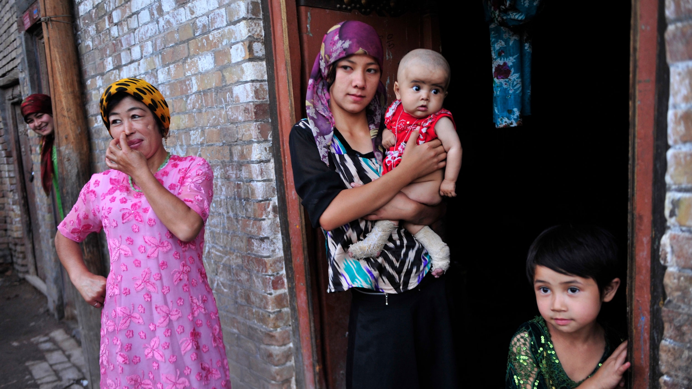 An ethnic Uighur woman hugs her son as she stands outside her house with her daughter and neighbors