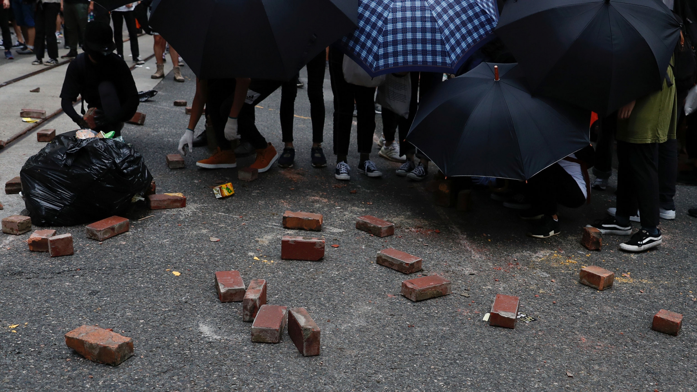 Anti-national security law protesters place bricks on road as a road block during a march at the anniversary of Hong Kong's handover to China from Britain in Hong Kong, July 1, 2020. A crowd of people hold umbrellas toward the camera with several bricks laying in the street.