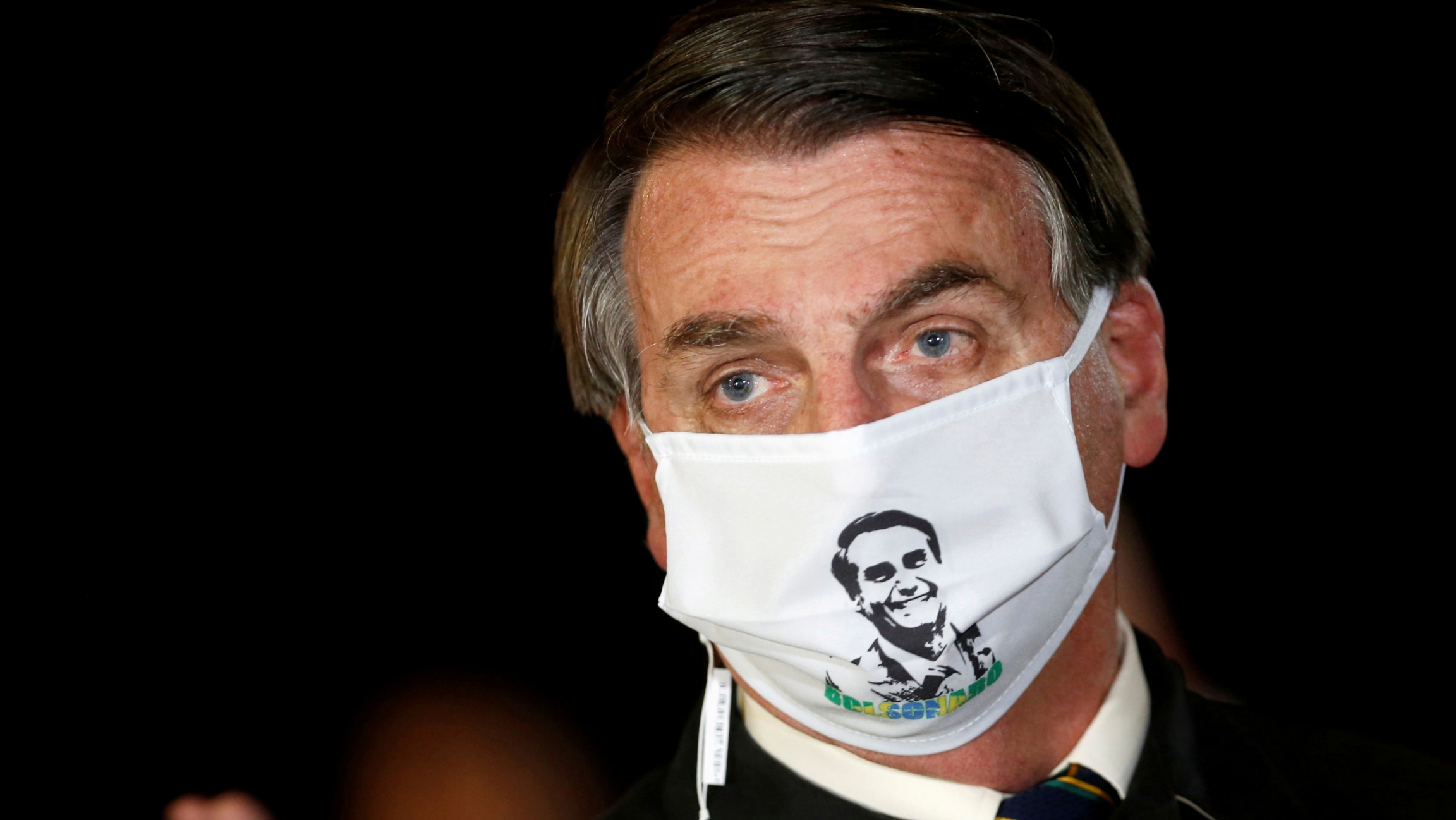 Brazil's President Jair Bolsonaro speaks with journalists while wearing a protective face mask amid the coronavirus outbreak, in Brasilia, Brazil, May 22, 2020. Brazil's President Jair Bolsonaro is shown wearing a white mask with his face printed on it.