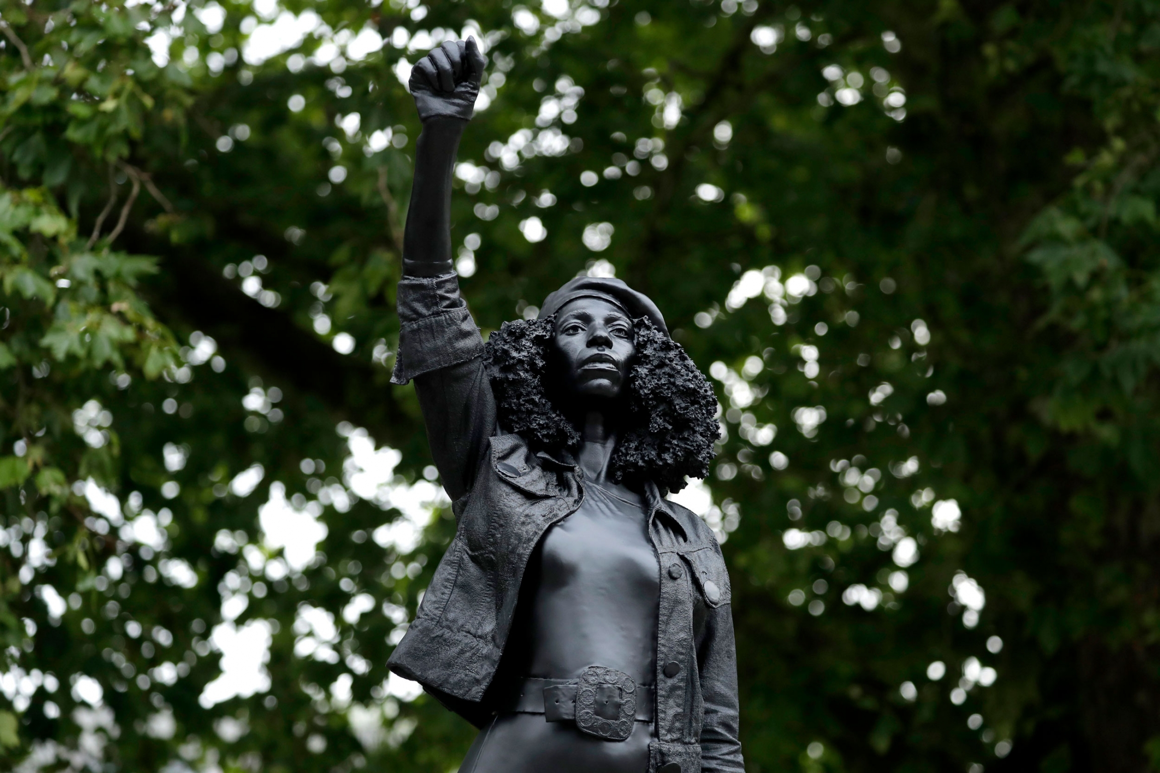 A close-up of the statue entitled "A Surge of Power (Jen Reid) 2020" by artist Marc Quinn in Bristol, England. A close-up of a dark statue showing a woman with curly hair, wearing a hat and holding her right fist in the air.