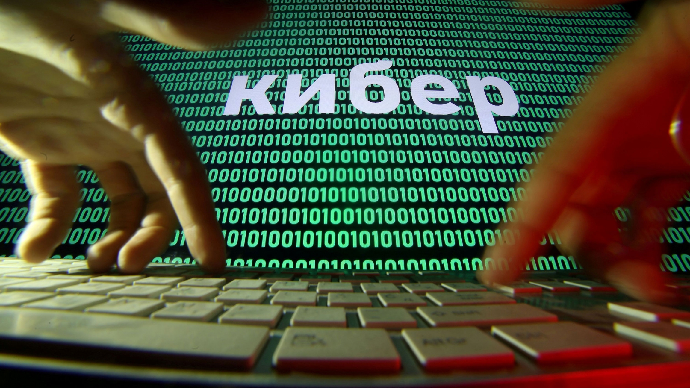 Hands are seen on a keyboard in front of a displayed code in this picture illustration. A screen is shown with green zeros and ones with a white keyboard in the nearground.