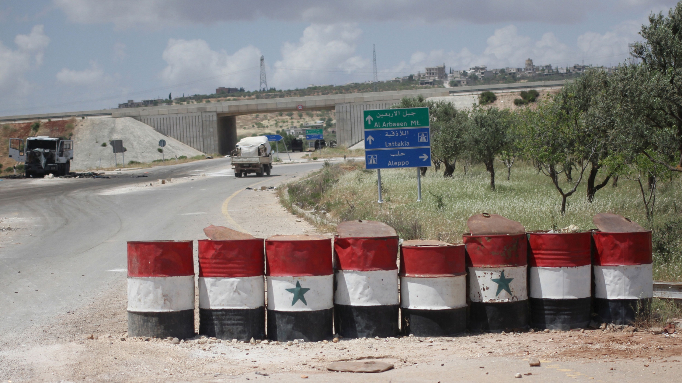 A view shows a checkpoint used by forces loyal to Syria's President Bashar al-Assad in the northwestern city of Ariha/ A road is shown with a row of large barrels with the colors of the Syrian flag painted on them.