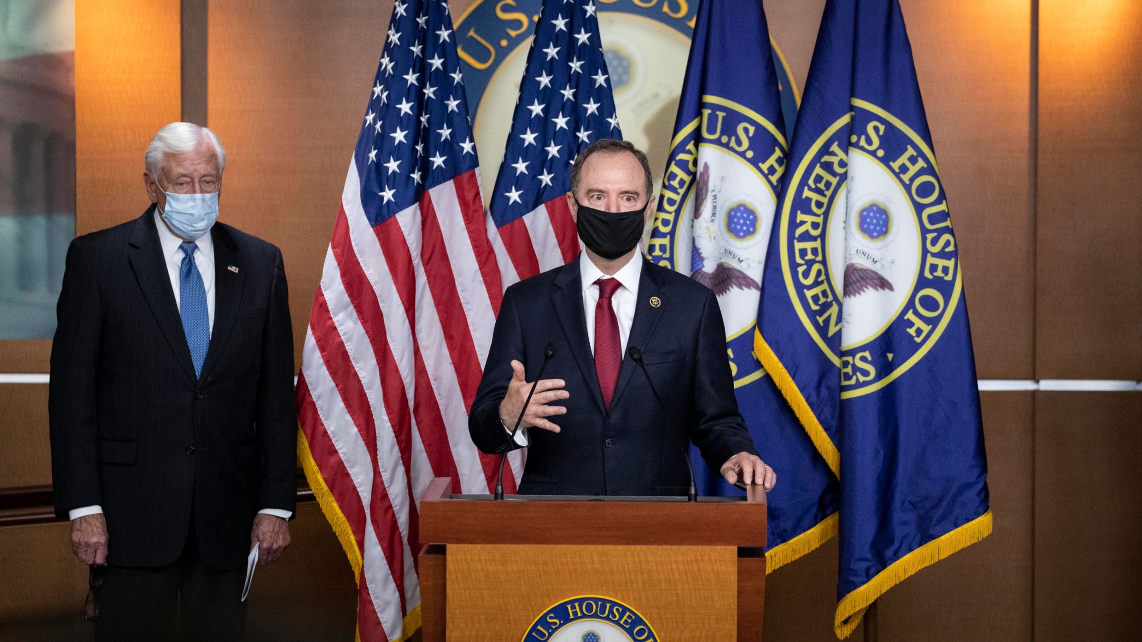 Rep. Adam Schiff, chairman of the House Intelligence Committee, right, speaks accompanied by House Majority Leader Steny Hoyer, during a news conference on Capitol Hill, after a meeting at the White House, Tuesday, June 30, 2020. Rep. Adam Schiff is shown wearing a black face mask and standing at a wooden podium with flags behind him.