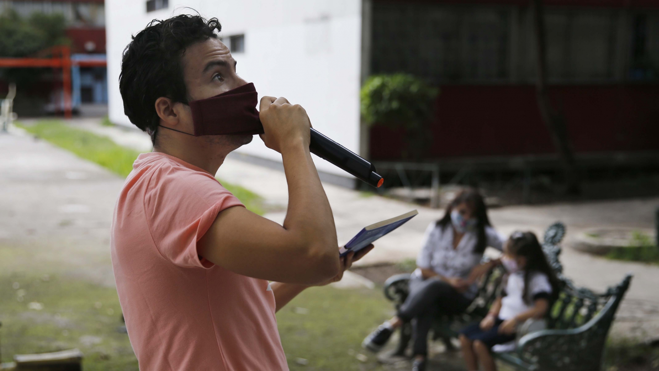 Residents listen from a bench, background, as Percibald García reads children's books aloud outside the high-rise buildings in the Tlatelolco housing complex, in Mexico City, on July 18, 2020. Residents listen from a bench, background, as Percibald García reads children's books aloud outside the high-rise buildings in the Tlatelolco housing complex, in Mexico City, on July 18, 2020.