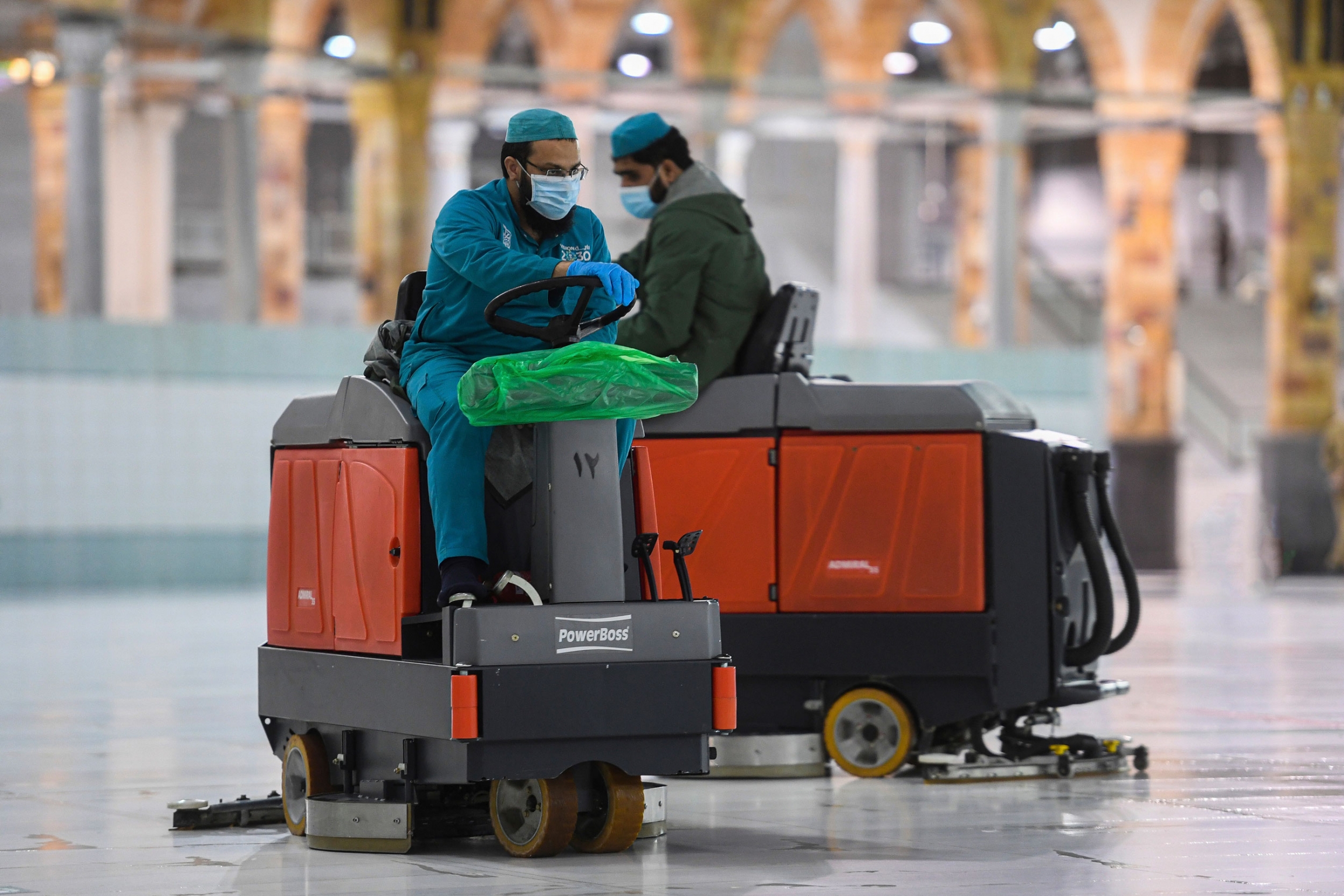 Workers polish the white marble floors surrounding Islam’s holiest site, the Kaaba. Two men are shown driving small machines that are polishing marble floors.