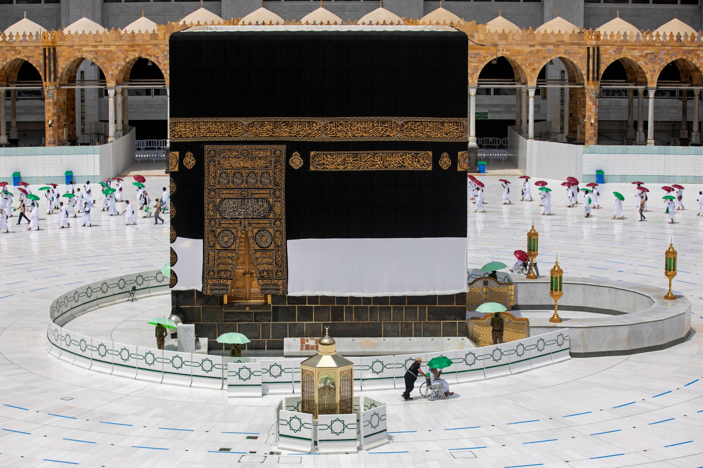 Pilgrims keep social distancing to limit exposure of the coronavirus, at the Grand Mosque in Mecca, Saudi Arabia. The cube-like Kaaba is shown center frame with a pilgrim being pushed in a wheelchair in the nearground.