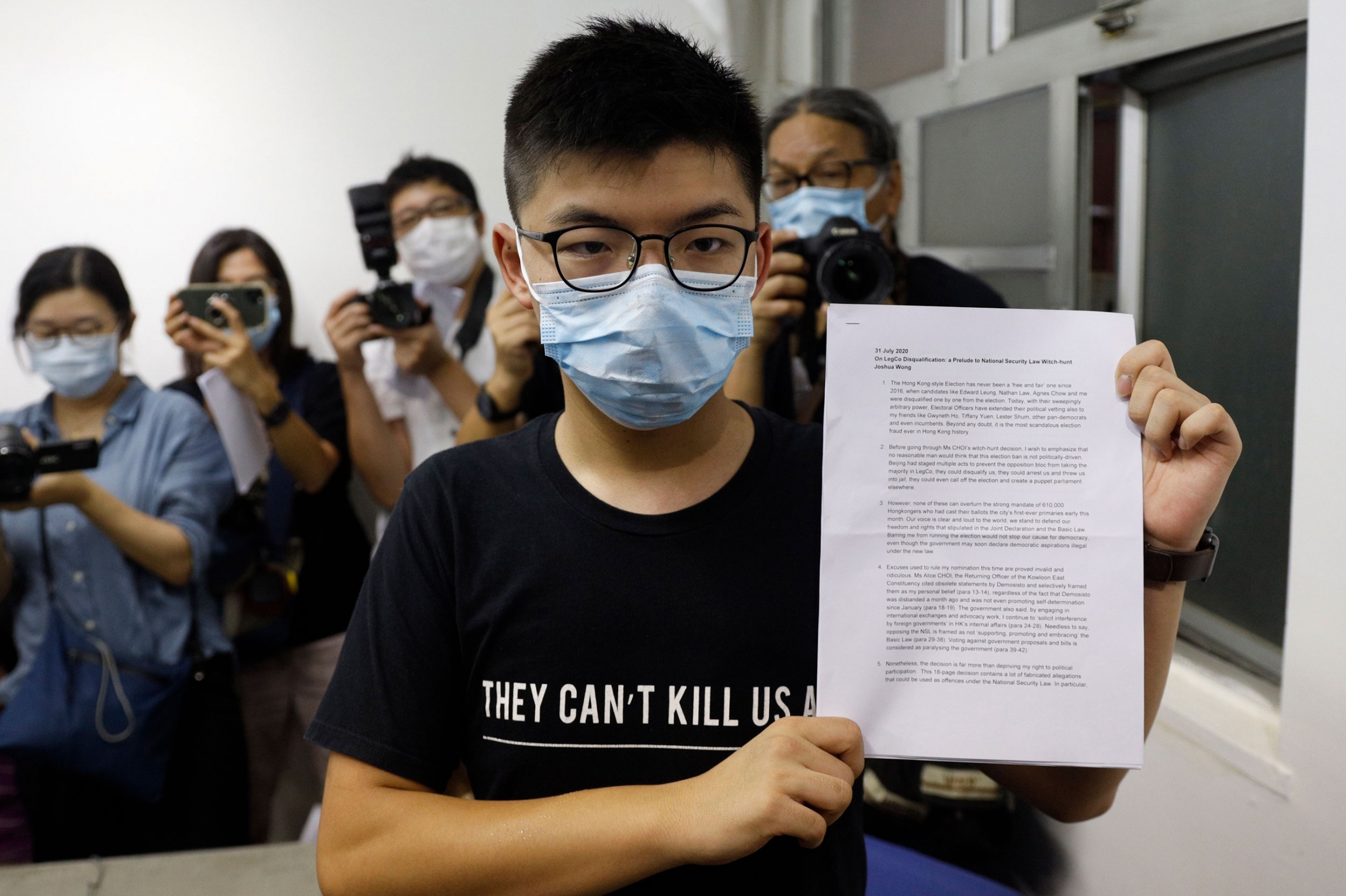Hong Kong pro-democracy activist Joshua Wong shows his disqualification notice during a press conference in Hong Kong, Friday, July 31, 2020. Hong Kong pro-democracy activist Joshua Wong is shown wearing a face mask a glasses while holding a white document up to the camera.