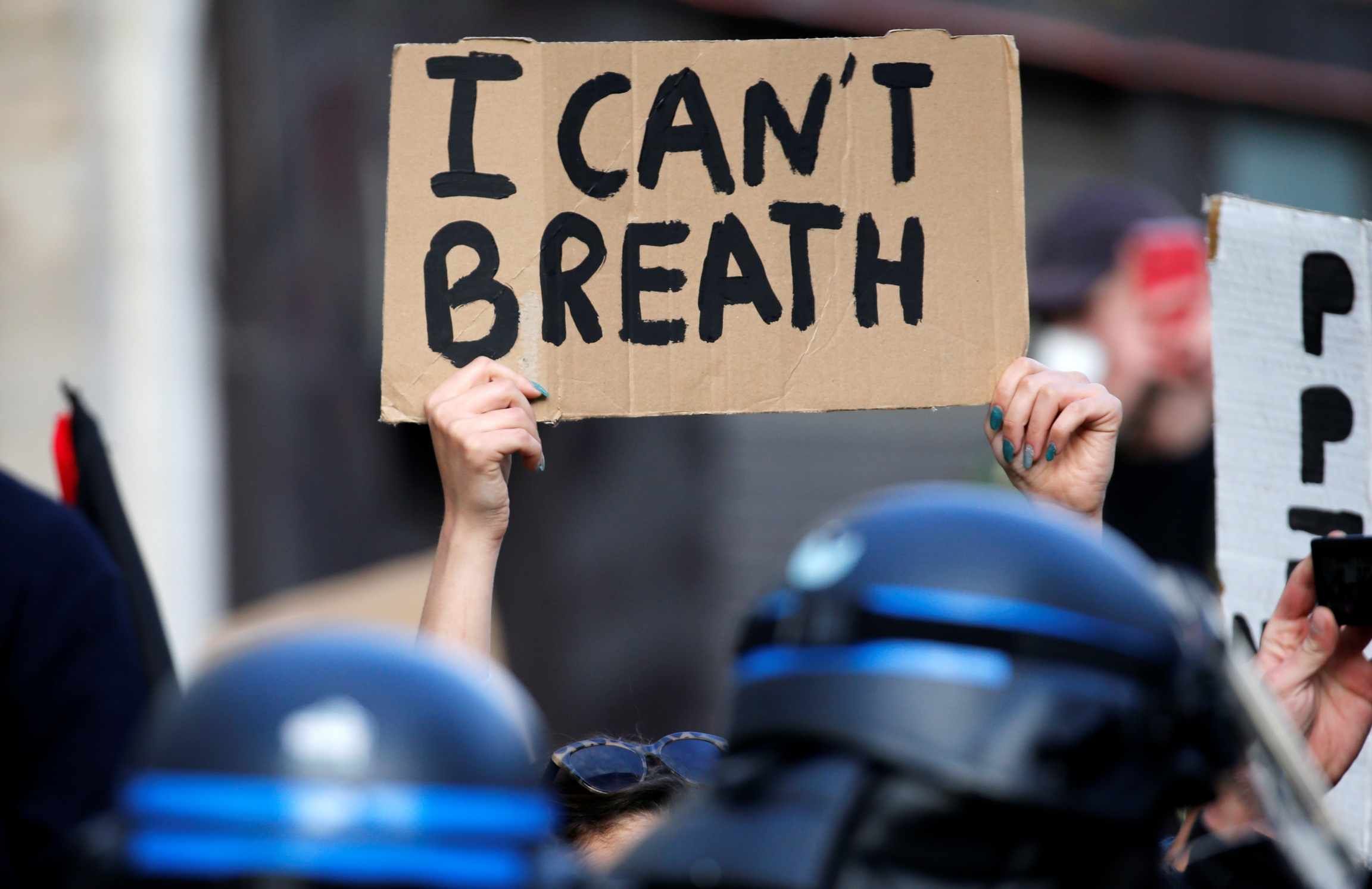 A protester holds a sign during a banned demonstration in memory of Adama Traoré, a 24-year-old black Frenchman who died in a 2016 police operation which some have likened to the death of George Floyd in the United States, on the Place de la Republique in A protester holds a sign on brown cardboard with the words "I can't breathe."