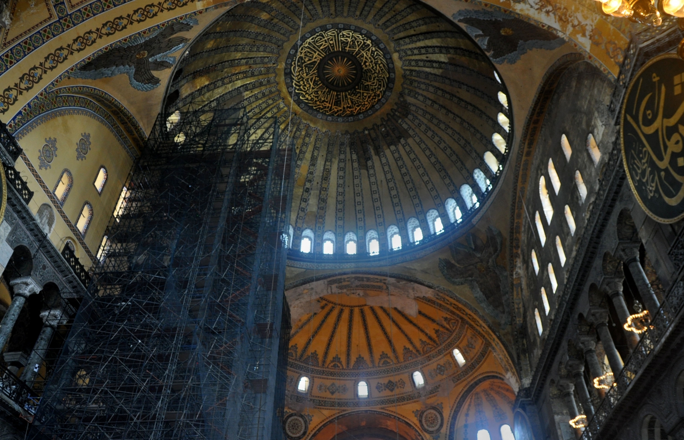 Inside Haghia Sophia, terraces of marble columns reach more than 100 feet above toward a striped, golden yellow and dark blue dome. The majestic dome of the Haghia Sophia with scaffolding for repairs