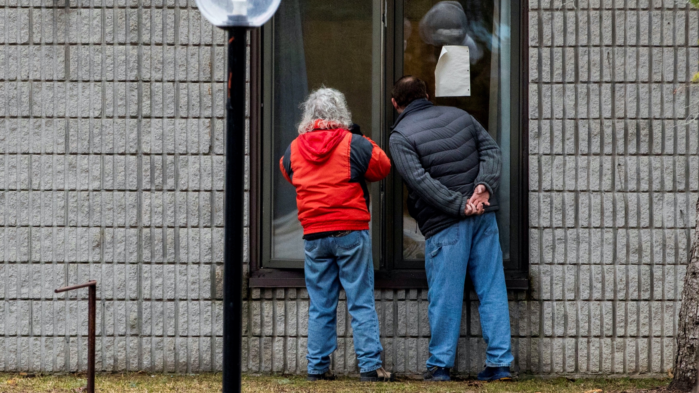Two people speak to a resident through a window at Pinecrest Nursing Home after several residents died and dozens of staff were sickened by coronavirus disease (COVID-19) in Bobcaygeon, Ontario, Canada, March 30, 2020. Two people stand outside a window peering inside a facility.