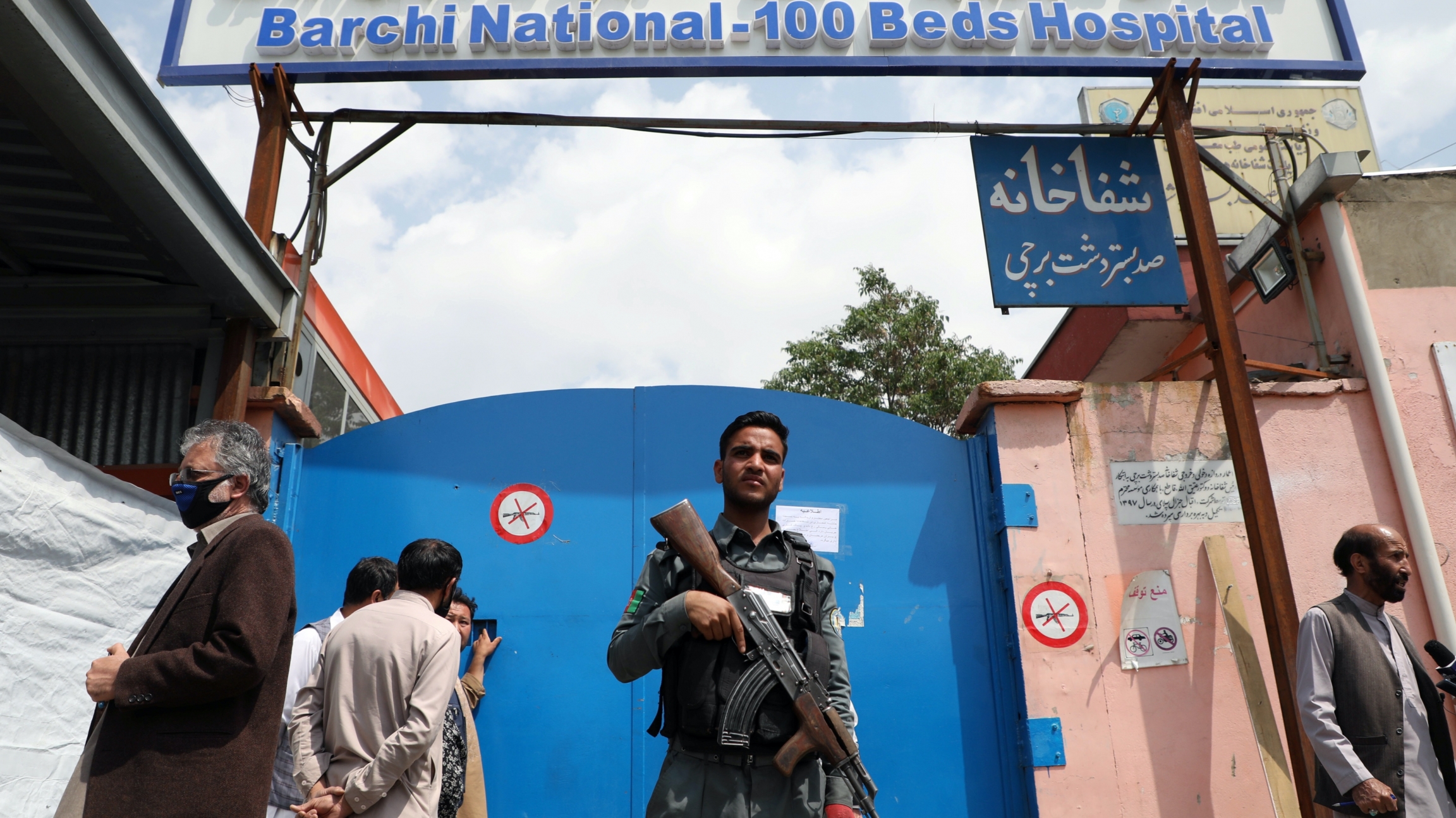 An Afghan policeman keeps watch outside of a hospital which came under attack in Kabul, Afghanistan, May 13, 2020. A man with a gun stands in front of a blue door of a hospital that got attacked.