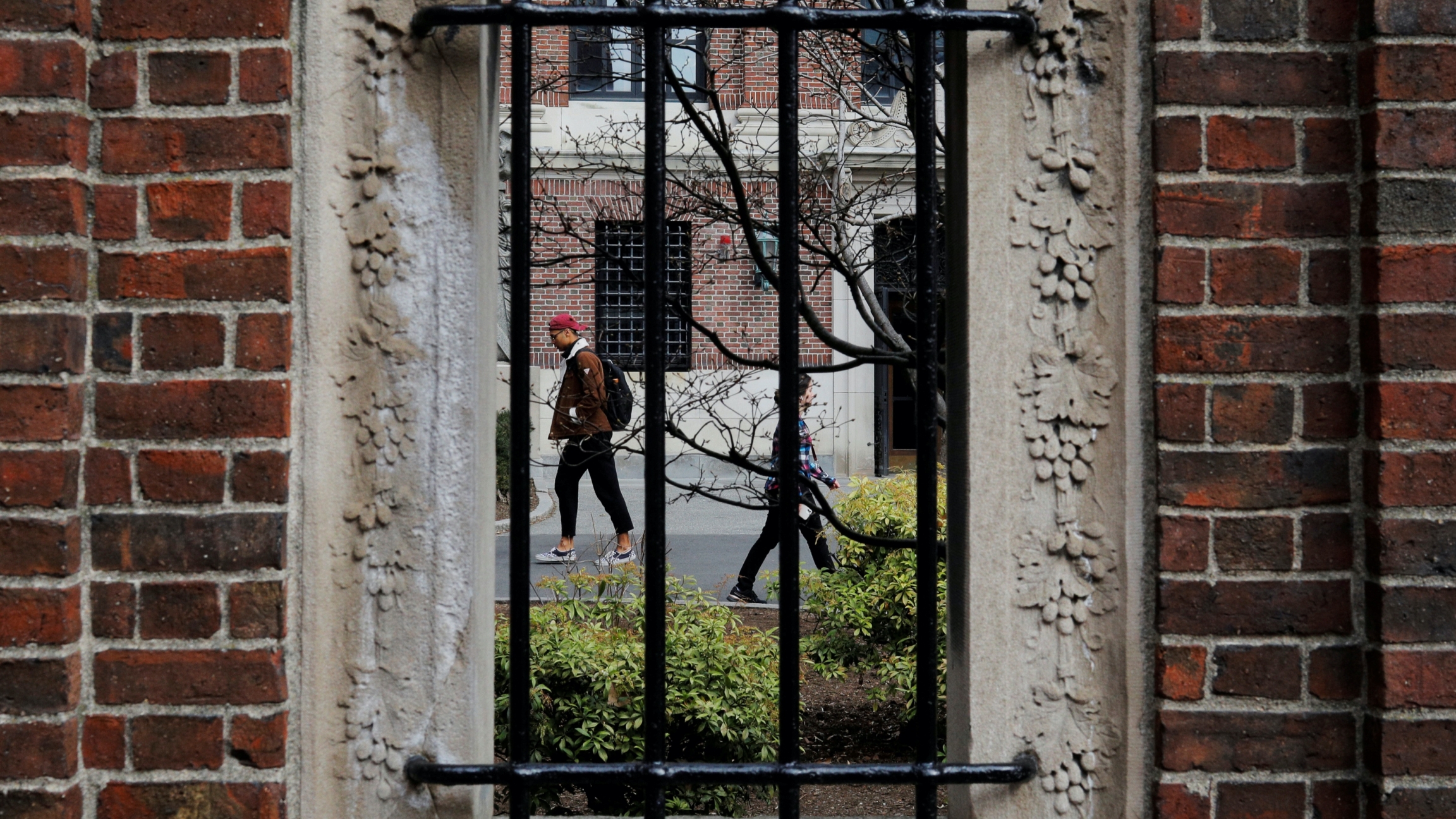Students and pedestrians walk through the Yard at Harvard University, after the school asked its students not to return to campus after Spring Break and said it would move to virtual instruction for graduate and undergraduate classes, in Cambridge, Massac Two students walk through a college campus