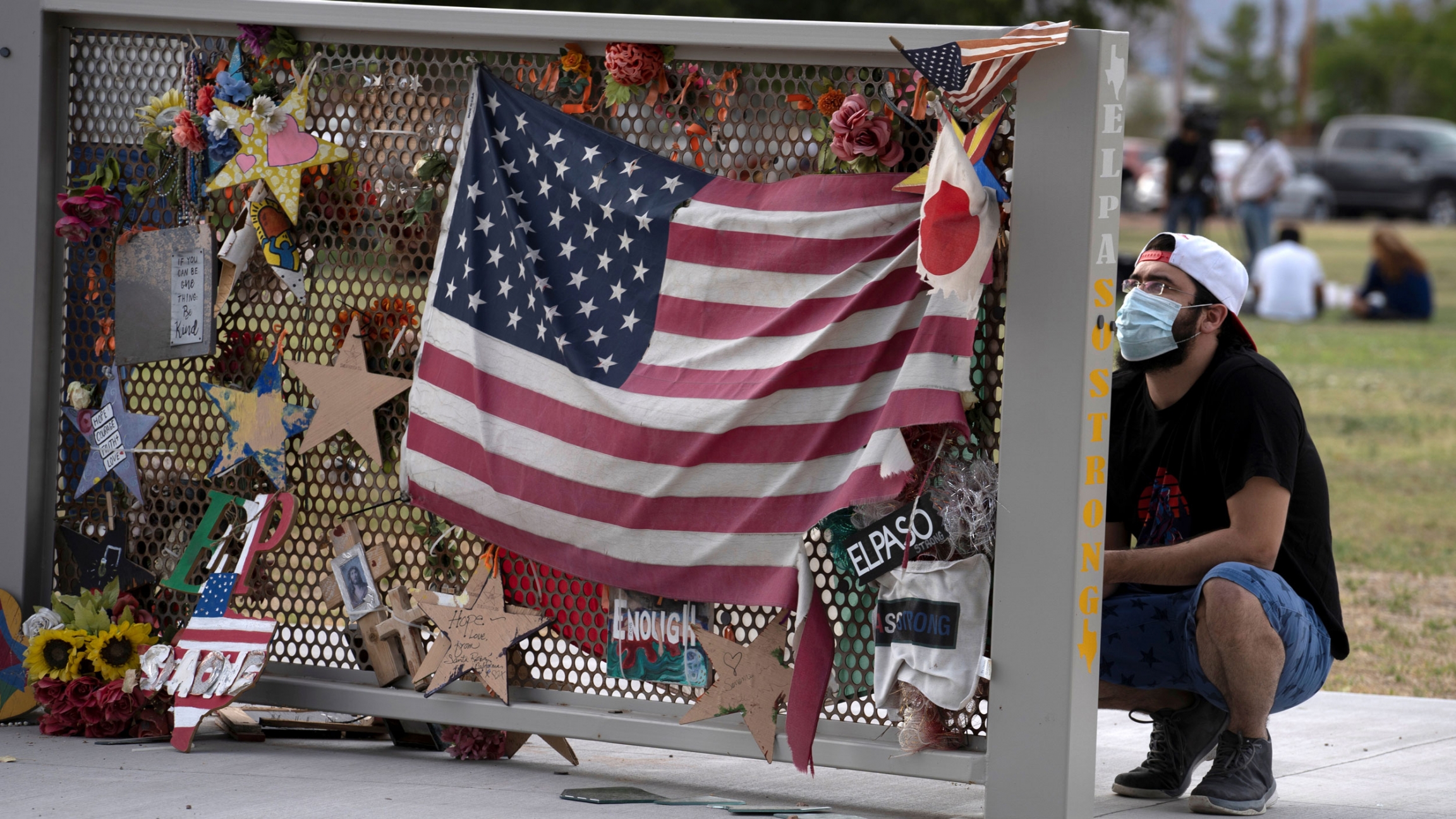 Isaac Chavira pays his respects at a memorial for the 23 victims of the Walmart shooting in Ponder Park in El Paso, Texas, August 2, 2020. A man is shown kneeling next to a memorial that has stars and an American flag pinned on it.